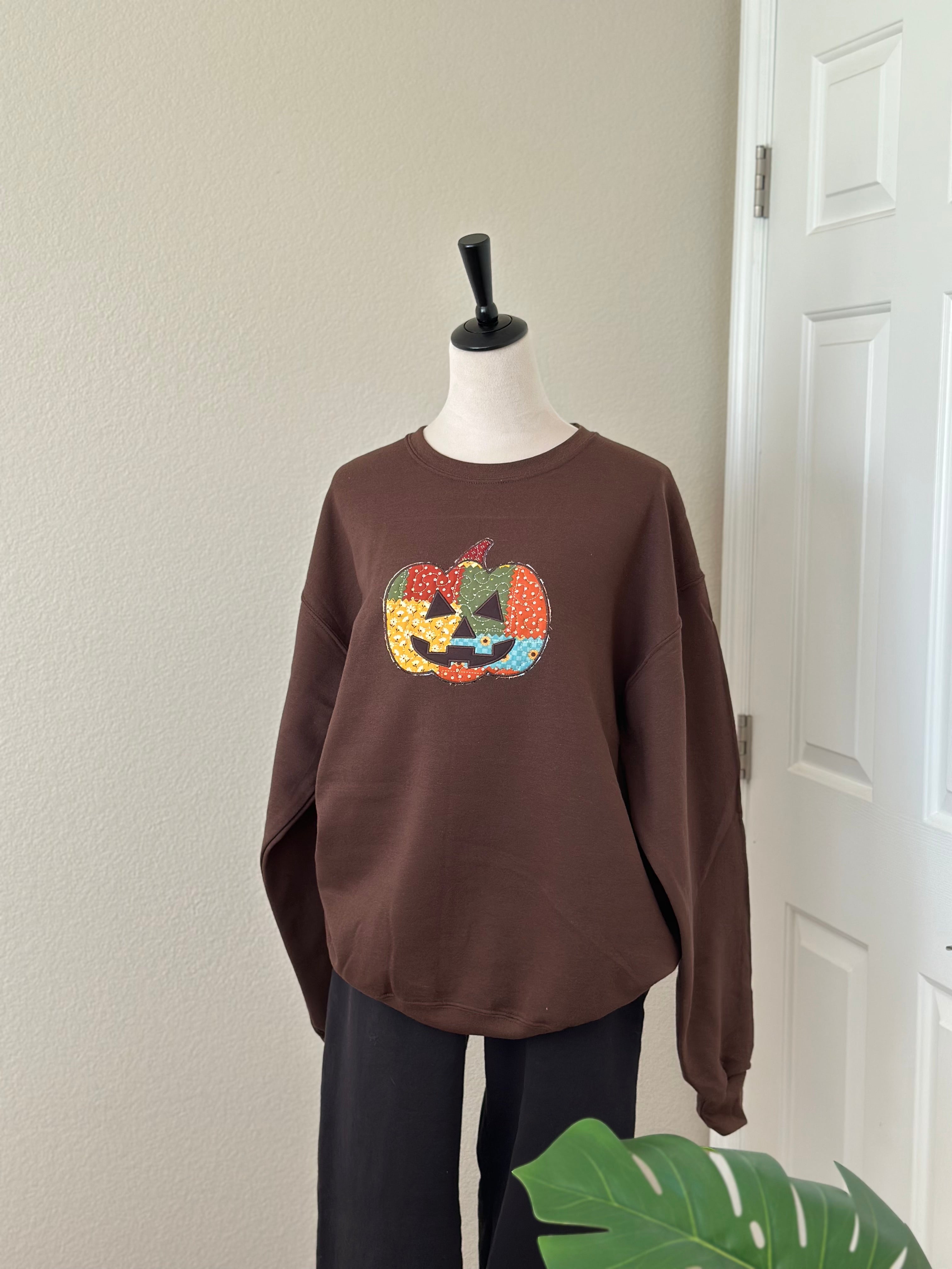 Full brown sweatshirt on mannequin featuring large embroidered patchwork jack-o’-lantern on chest.