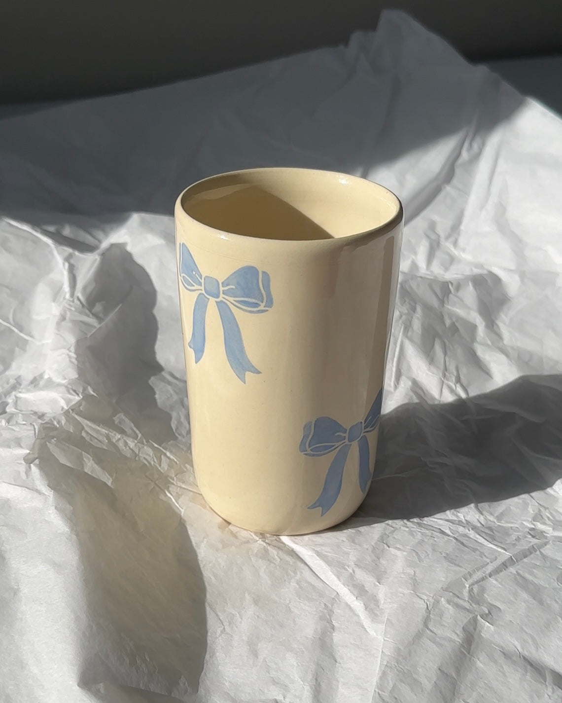 Handmade stoneware coffee mug with soft blue bow design on cream glaze, photographed in natural light for a coquette aesthetic
