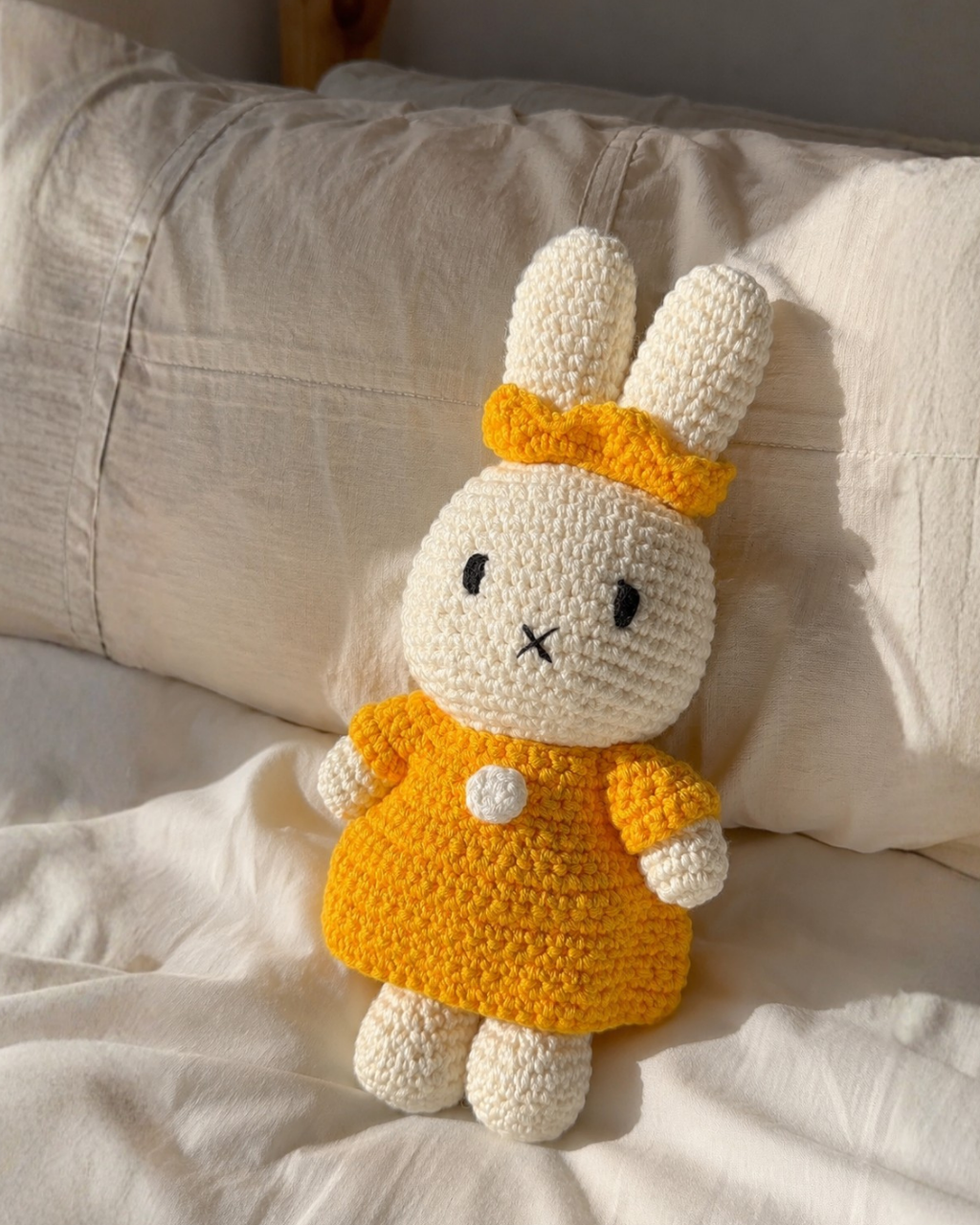 Handmade Miffy bunny plush in her Yellow Dress & Crown, resting on linen pillows on a sunlit bed.