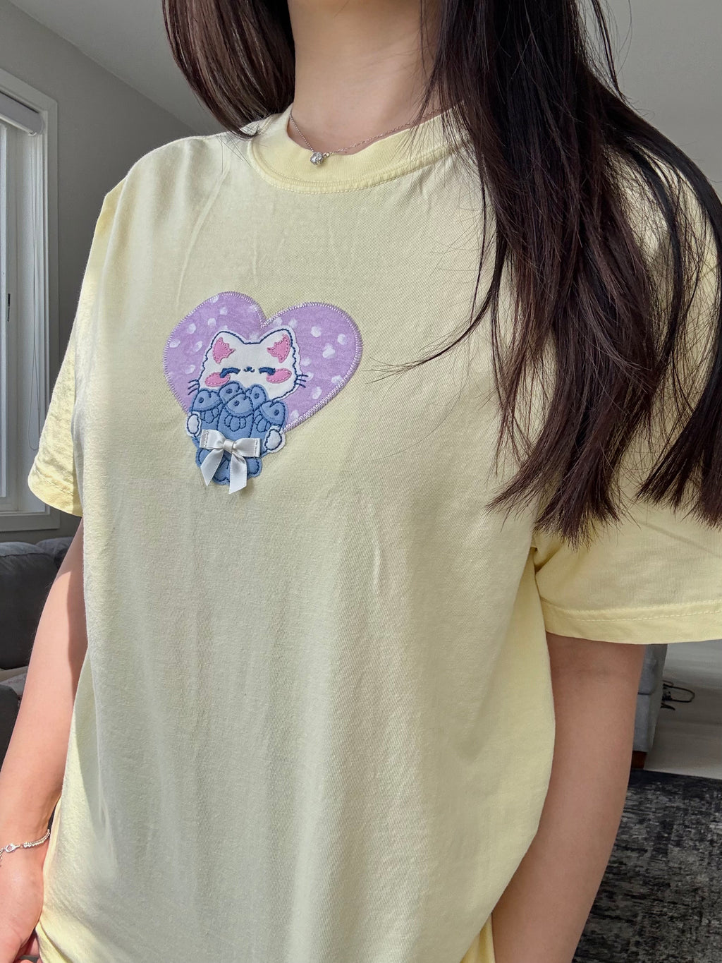 Close-up of handmade embroidered cat patch with satin bow on pastel yellow Comfort Colors t-shirt.
