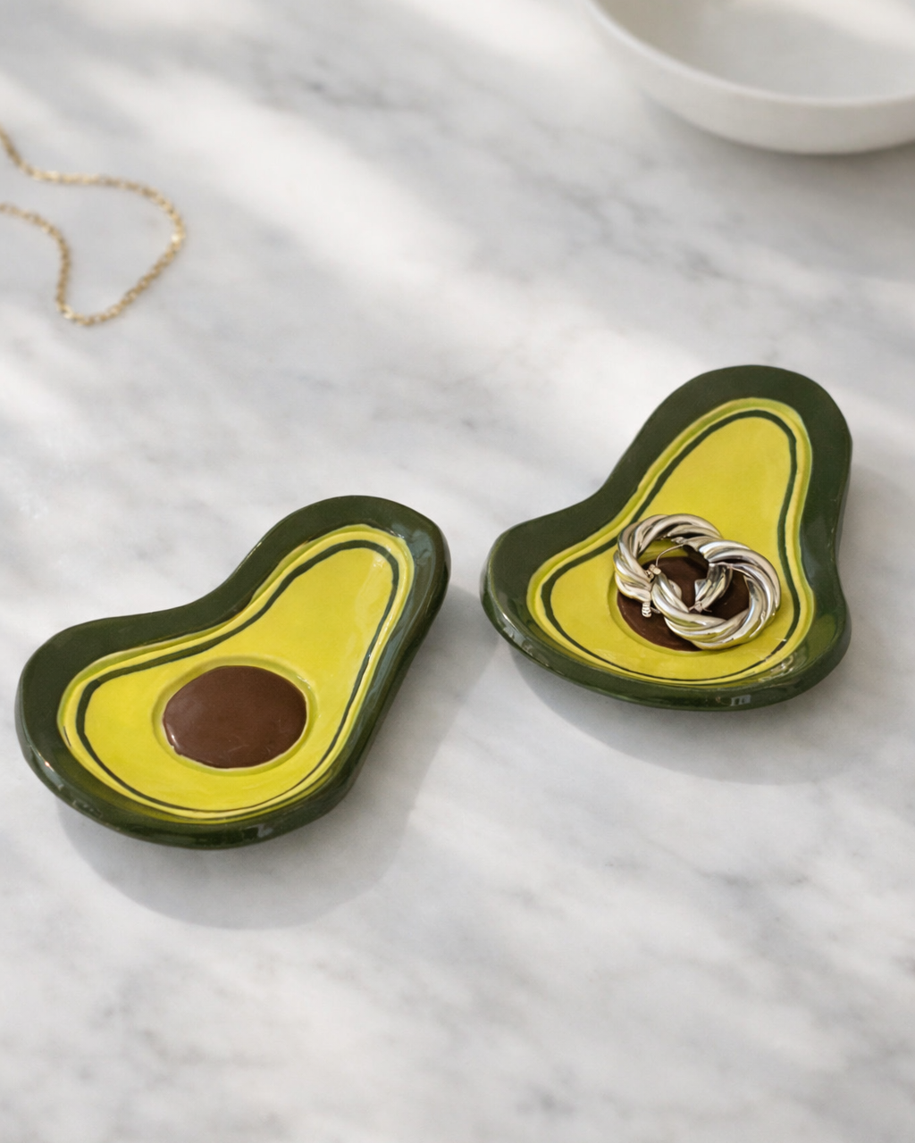 Handmade ceramic avocado trinket dish holding rings on marble surface, fruit shaped jewelry holder for vanity organization and bathroom counter decor