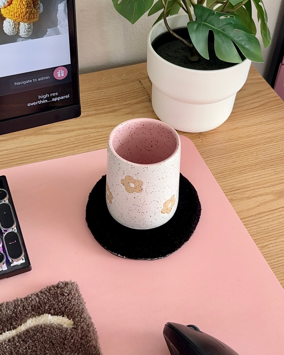 Handmade speckled stoneware coffee mug with stamped daisy design and blush pink interior, styled on a cozy desk setup
