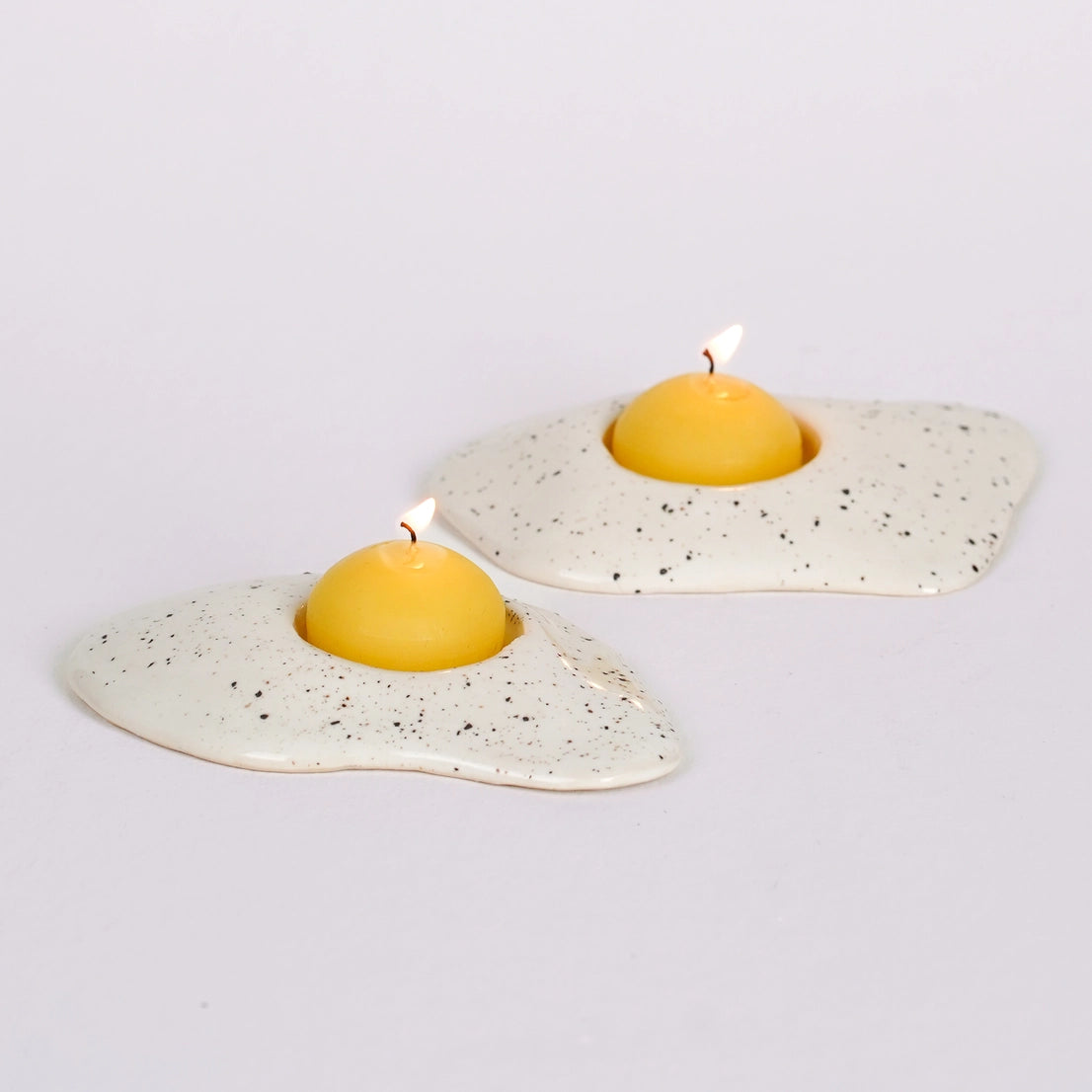Two handmade ceramic egg candle holders with lit beeswax yolk tealights, styled for display
