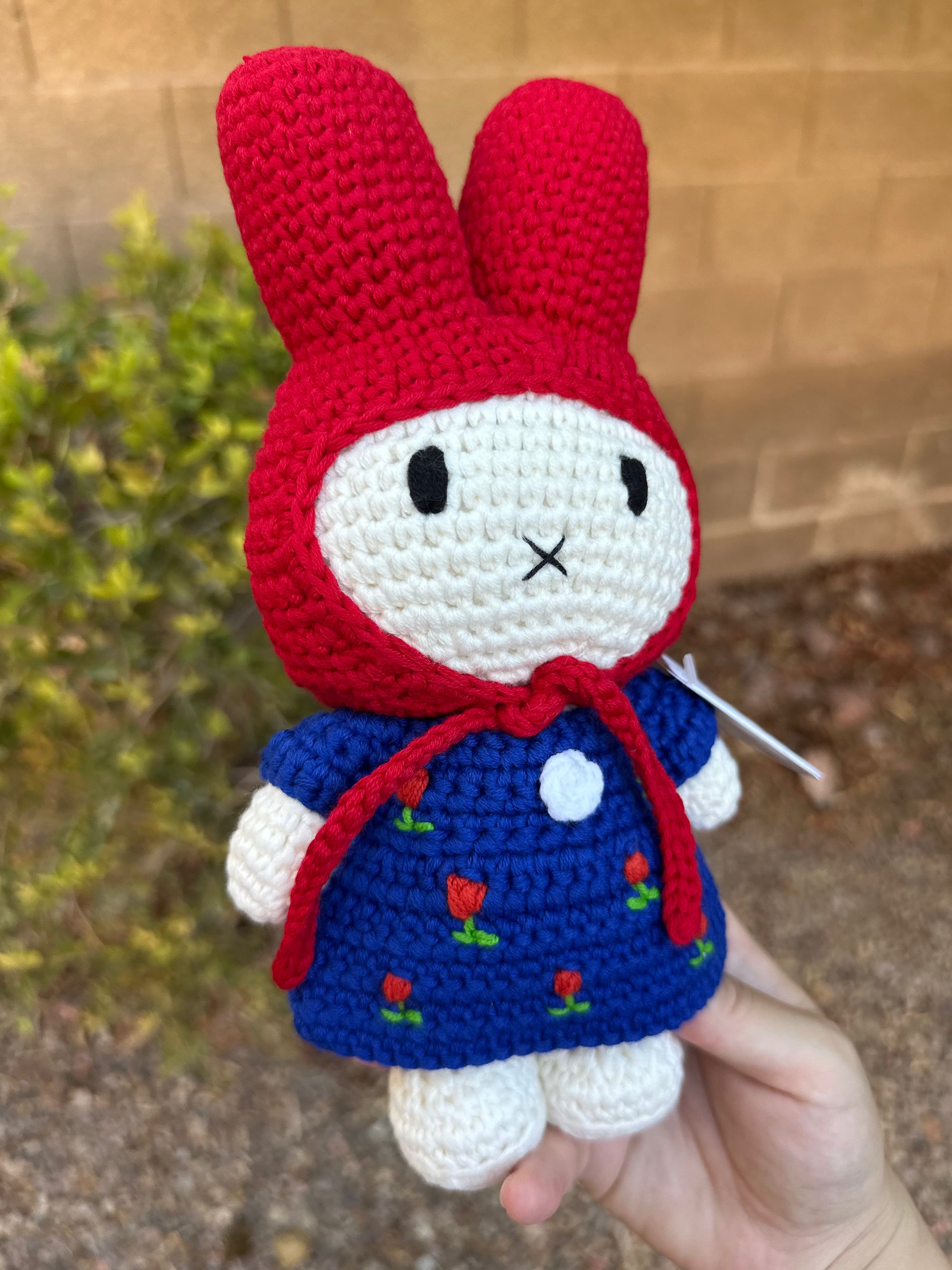 Side view of Miffy crochet plush in tulip dress and red hood, held outside.