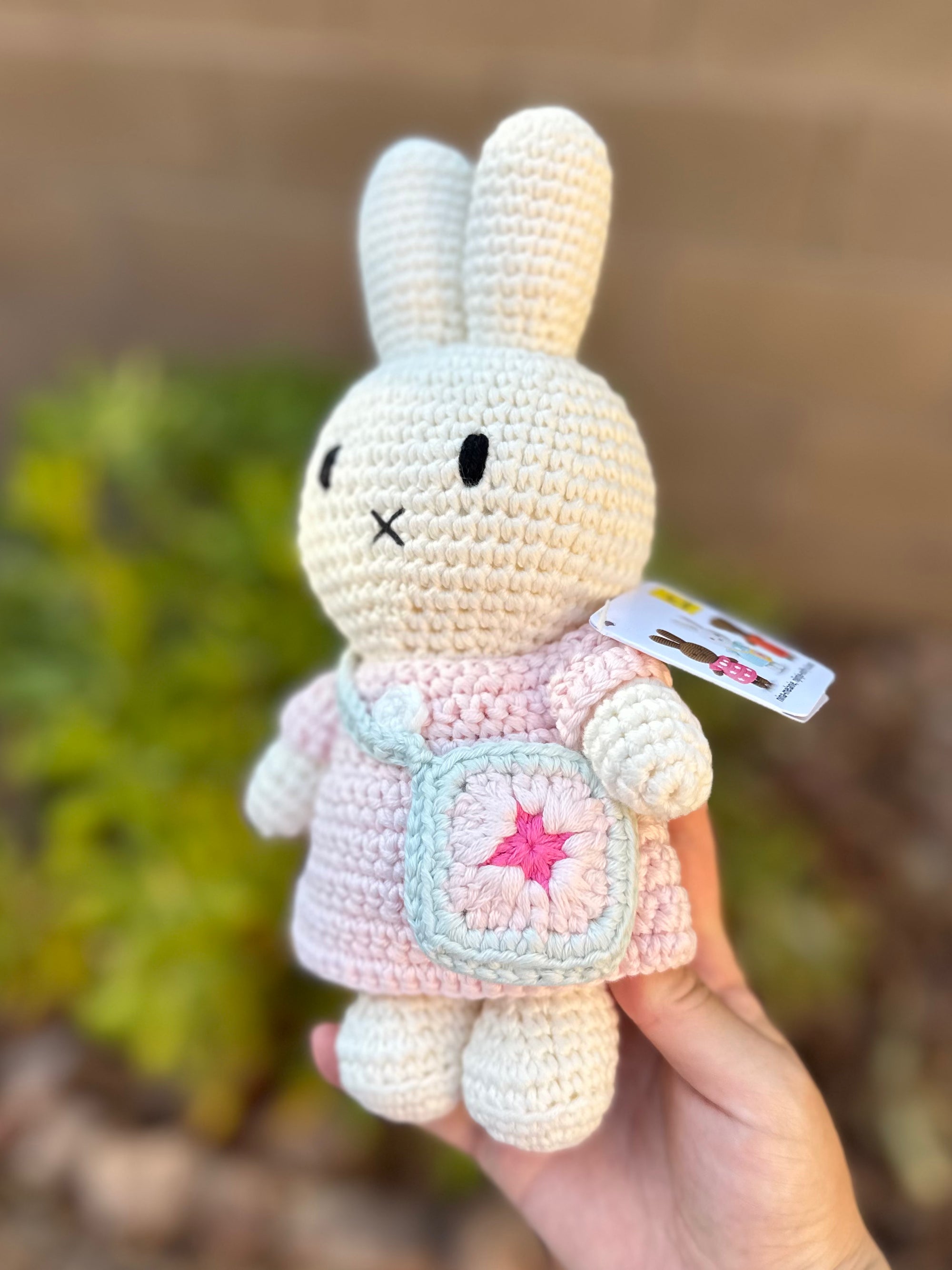Side view of handmade Miffy crochet plush wearing a pastel pink dress and crochet blue bag with a flower design.