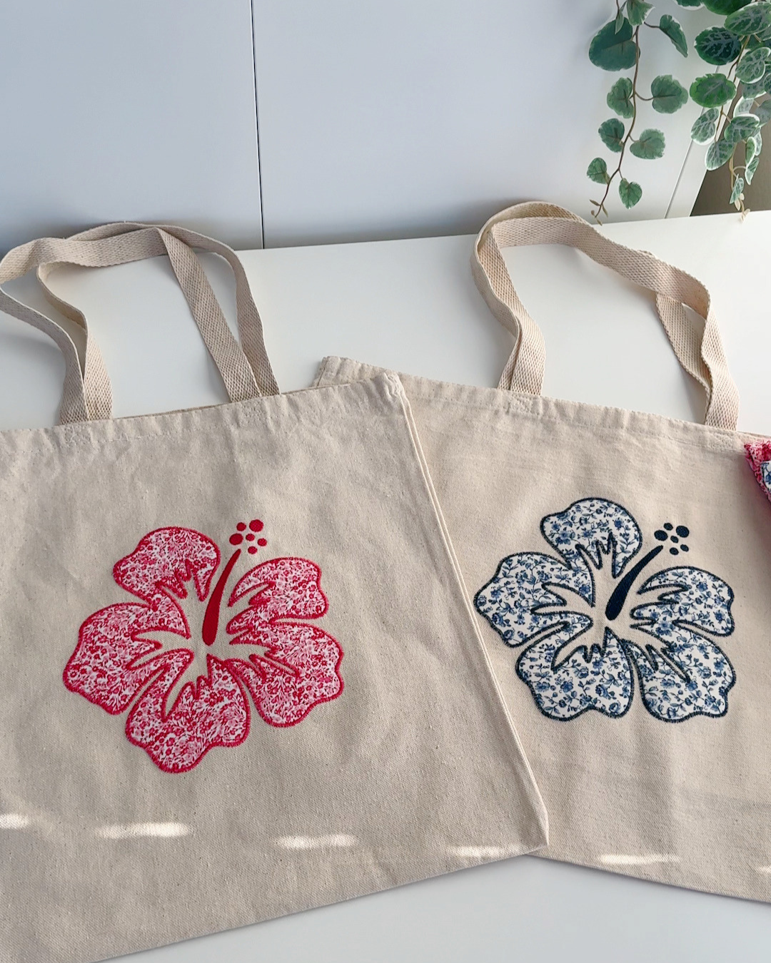 Pink and navy hibiscus embroidered canvas tote bags side by side, floral patchwork aesthetic everyday totes