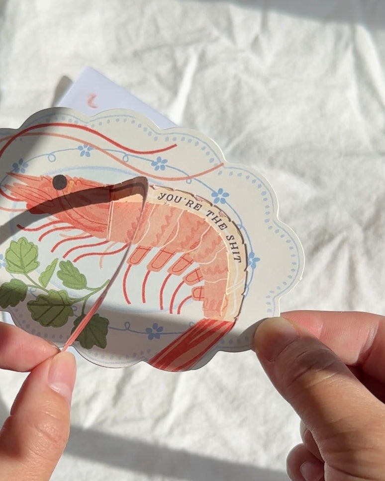 Interactive shrimp greeting card being pulled to reveal “You’re the sht” message.