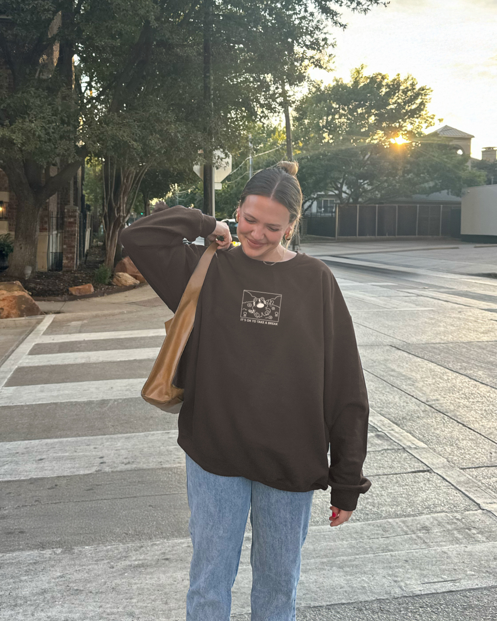 Brown sweatshirt with ‘It’s OK to take a break’ tiger design, worn outdoors with jeans and shoulder bag during golden hour