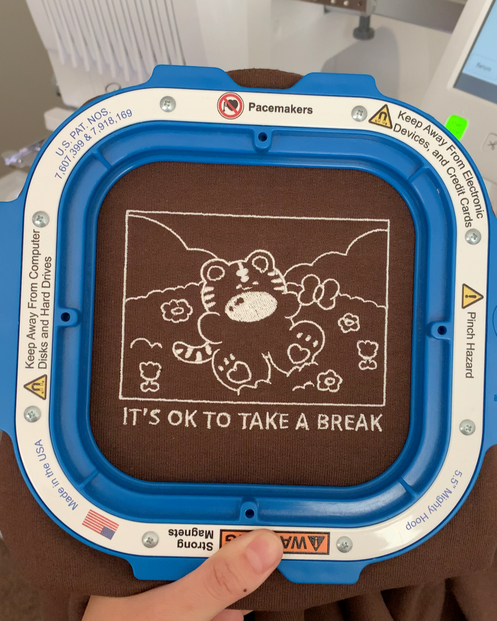 Close-up of embroidery machine stitching ‘It’s OK to take a break’ tiger design on brown sweatshirt, small biz behind-the-scenes view