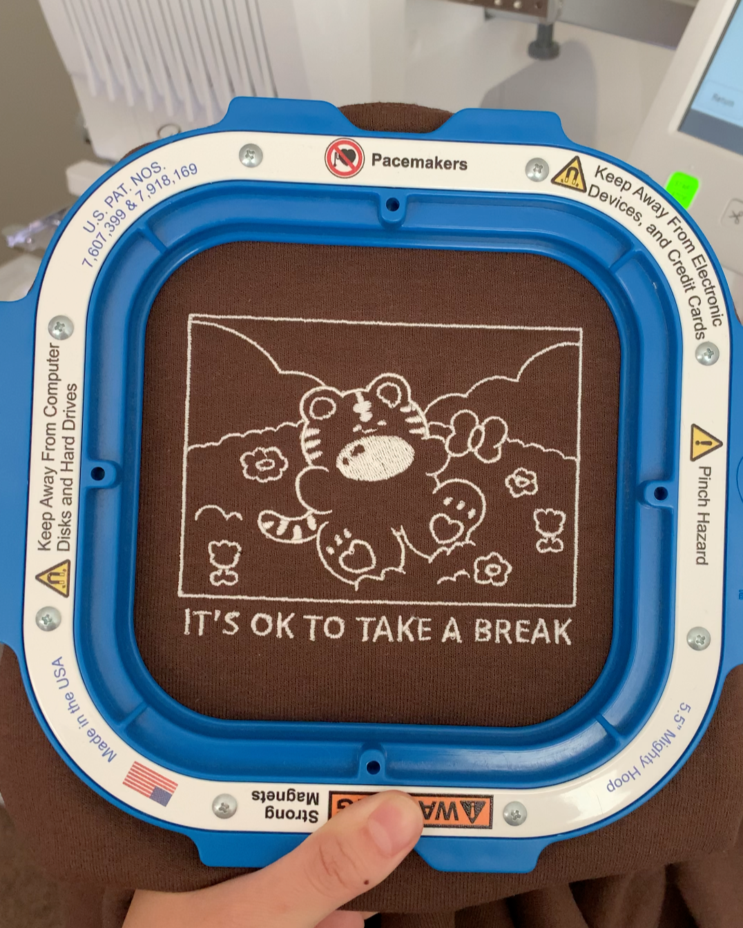 Close-up of embroidery machine stitching ‘It’s OK to take a break’ tiger design on brown sweatshirt, small biz behind-the-scenes view