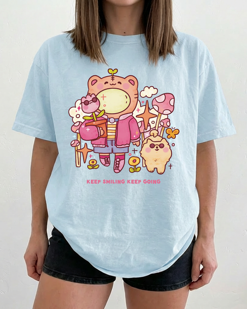 Light blue graphic t-shirt featuring a cheerful illustrated bear and the phrase “keep smiling keep going” on the front