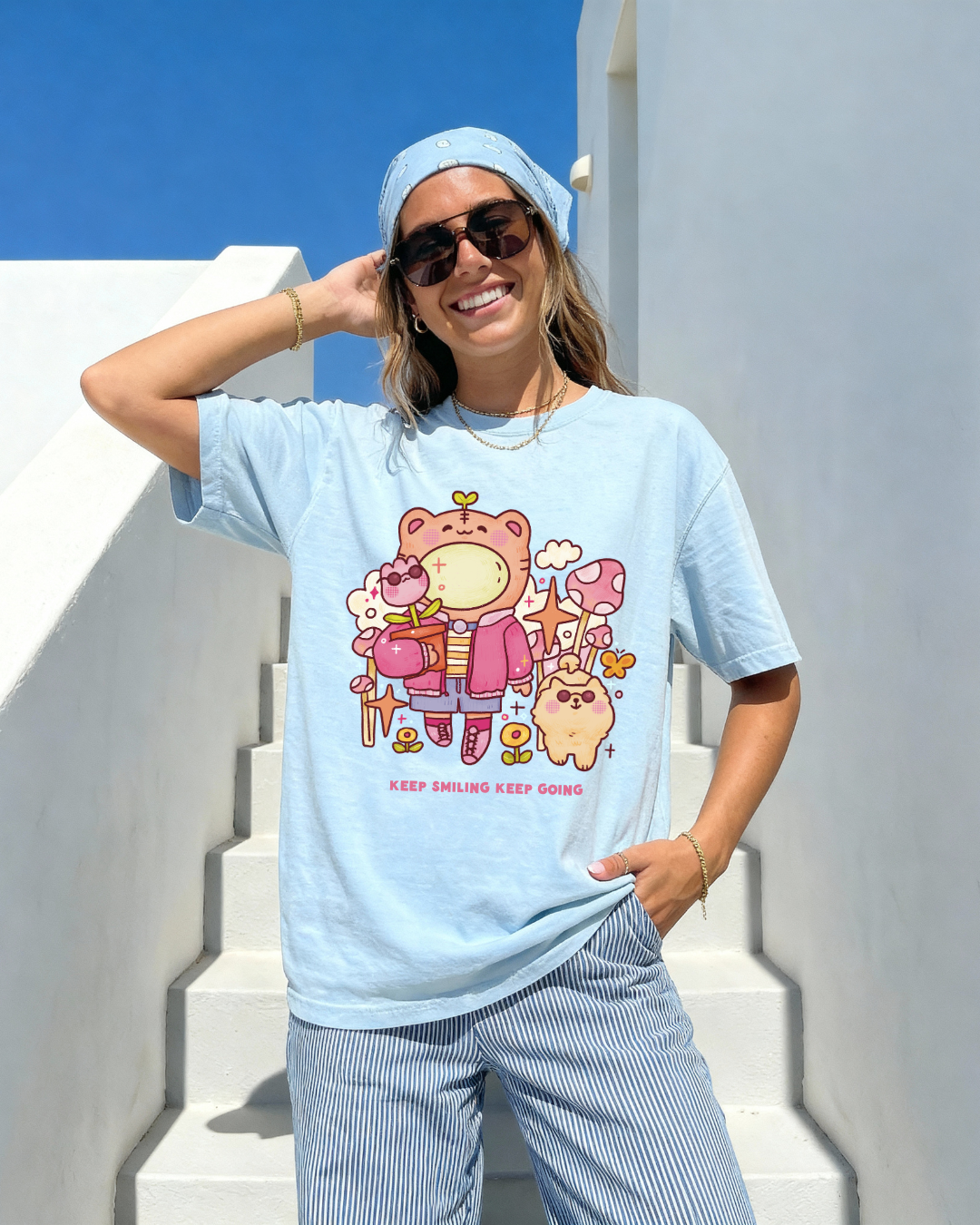 Woman wearing a light blue “keep smiling keep going” graphic tee with a playful illustrated bear design outdoors in bright sunlight