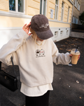 Cream sweatshirt with ‘Life is better with you’ embroidered cartoon design, styled with black bag and iced coffee during casual city stroll