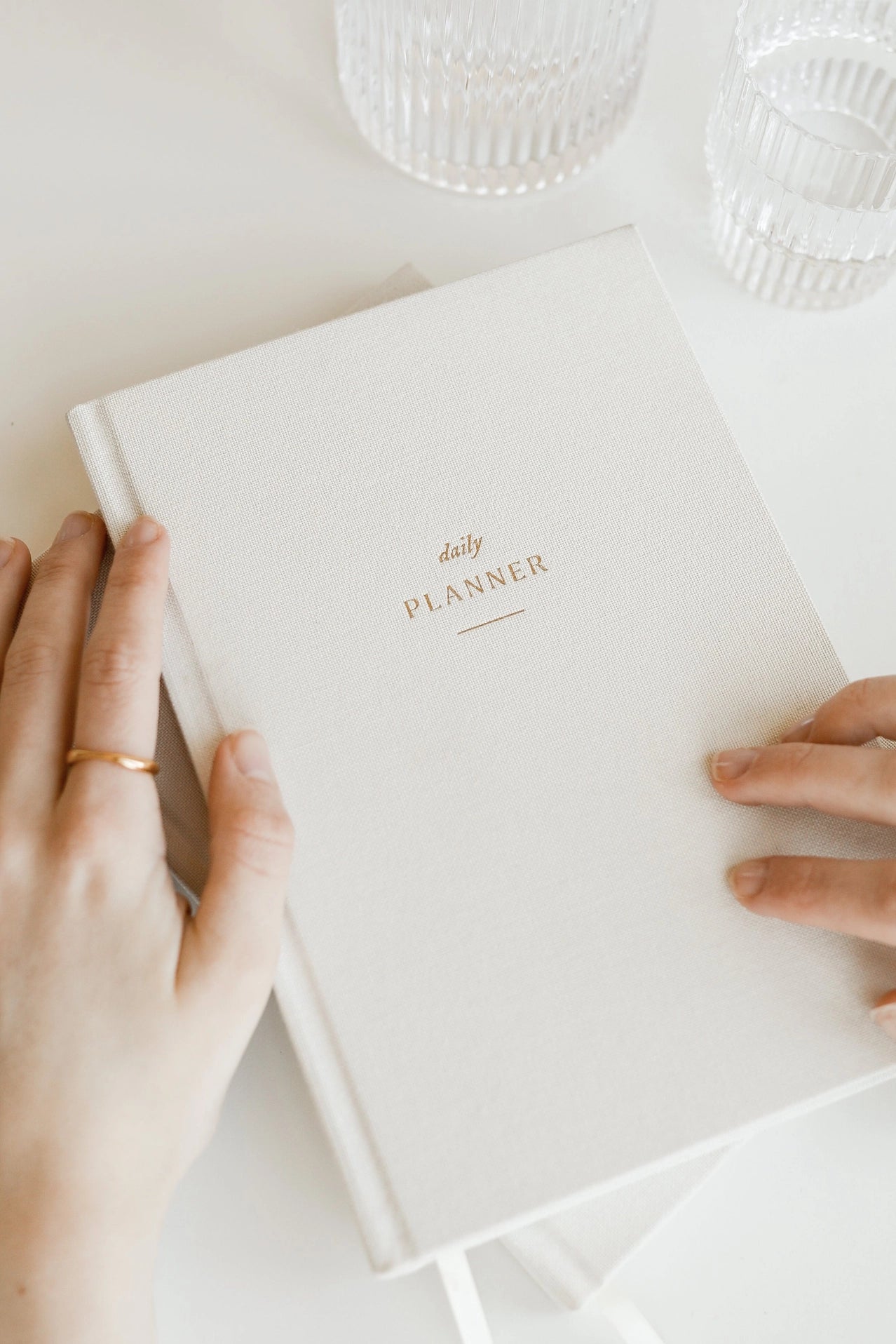Hands holding a beige linen hardcover undated daily planner with subtle gold foil lettering, highlighting texture and premium materials.