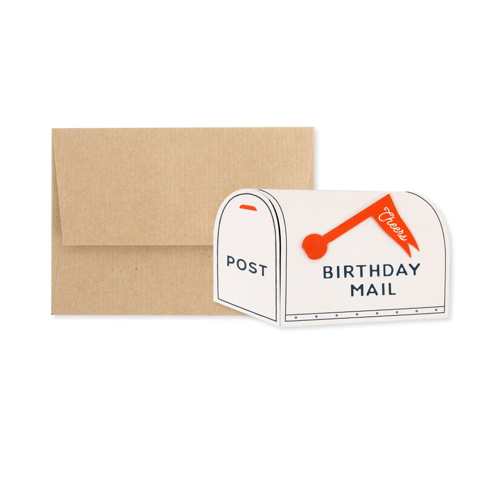 Flat-lay image of a charming mailbox-shaped birthday card with a red flag that says “Cheers,” paired with a recycled kraft envelope. A unique and playful snail mail card perfect for birthdays.

