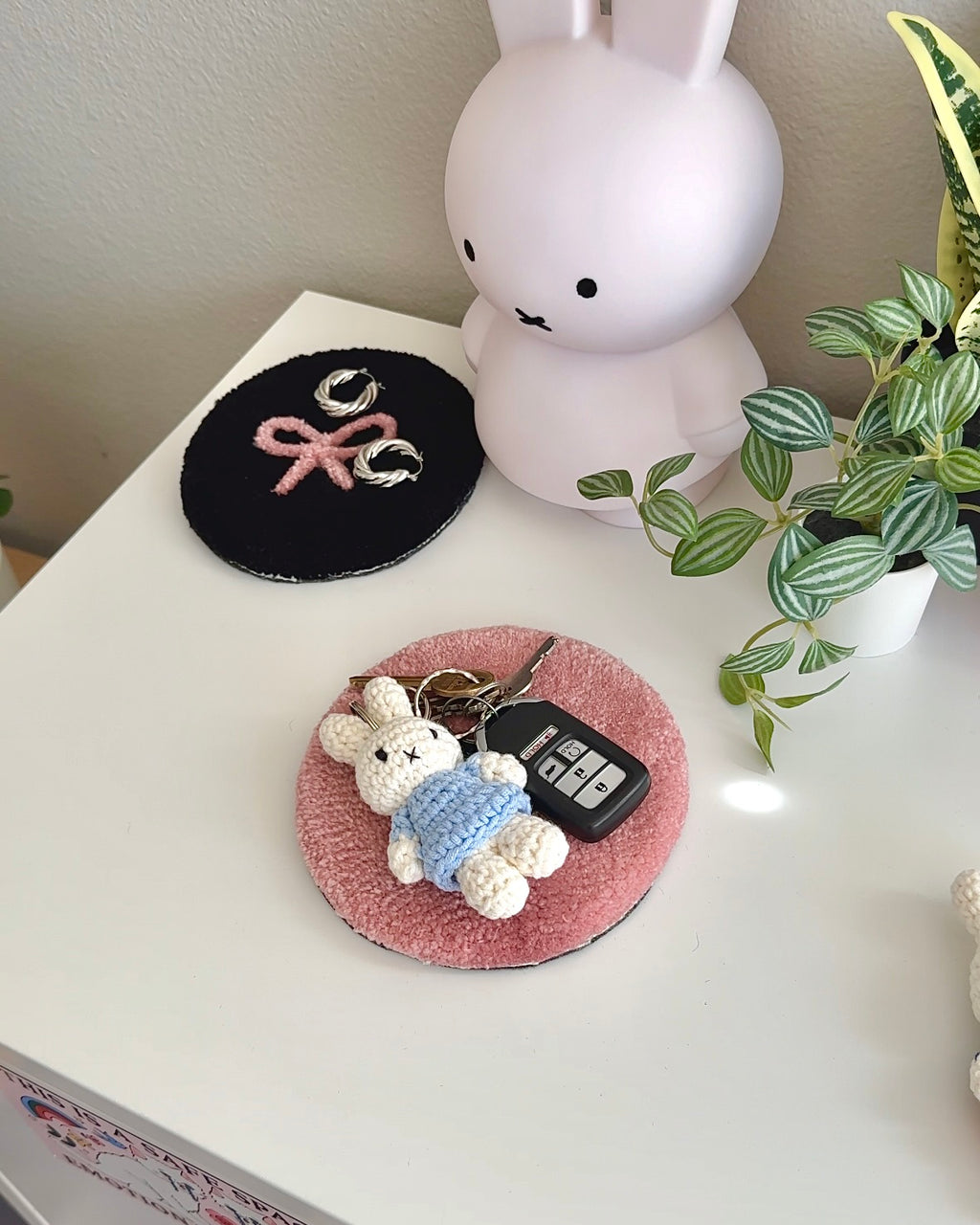 Miffy crochet keychain in a baby blue dress resting on a tray with keys, handmade cotton bag charm used as a soft everyday carry item.