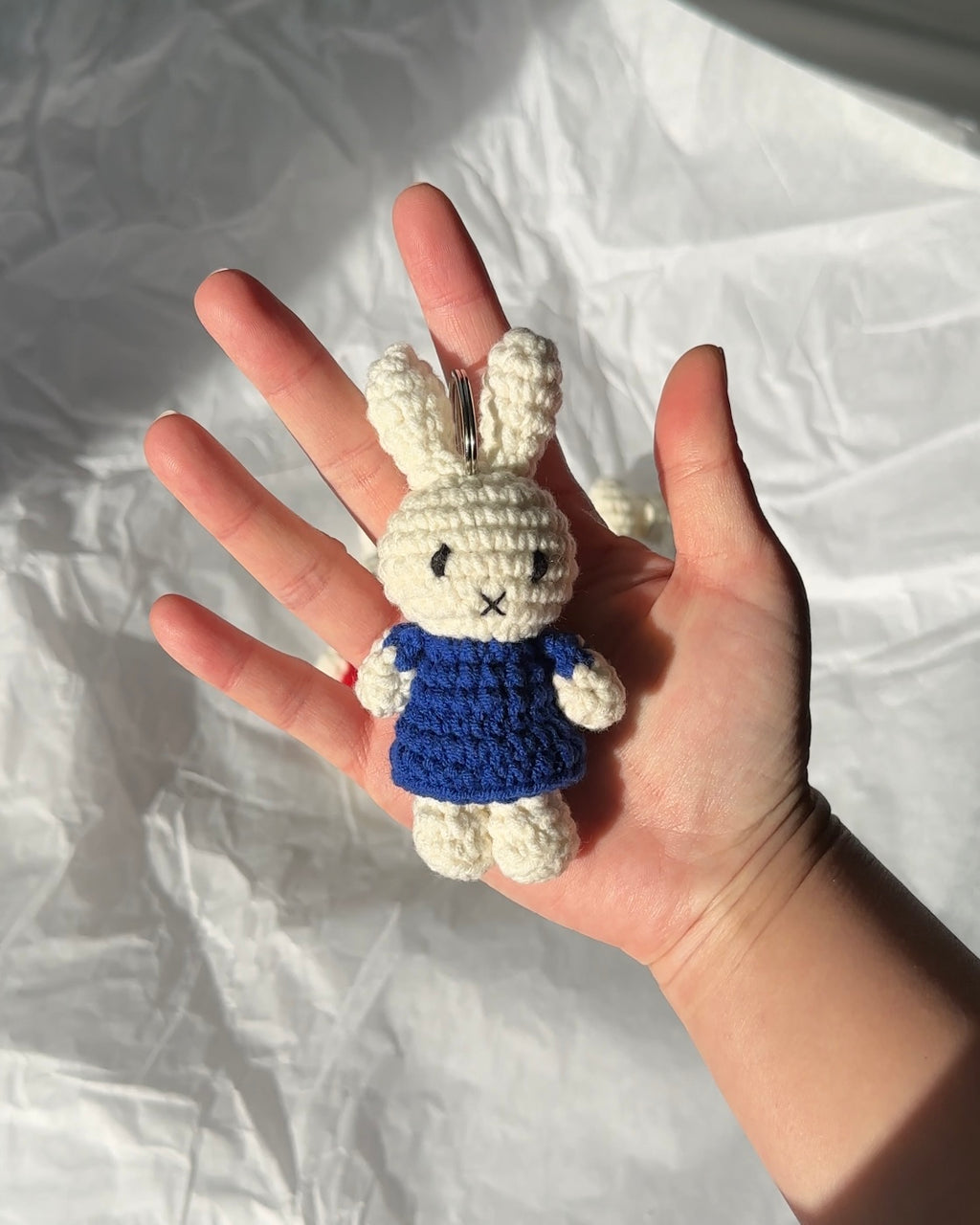 Miffy crochet keychain in a navy blue dress made from cotton yarn, held in hand in natural light, soft and lightweight bag charm.