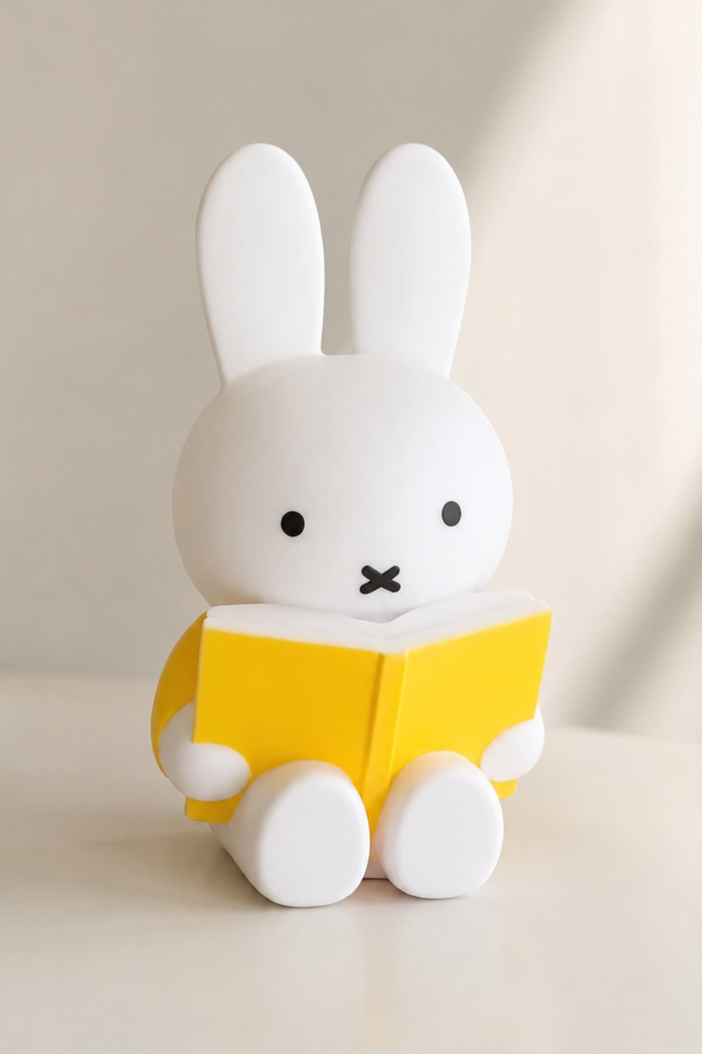 Miffy coin bank with yellow book against a soft neutral background with natural light shadow, a minimalist aesthetic decor piece.
