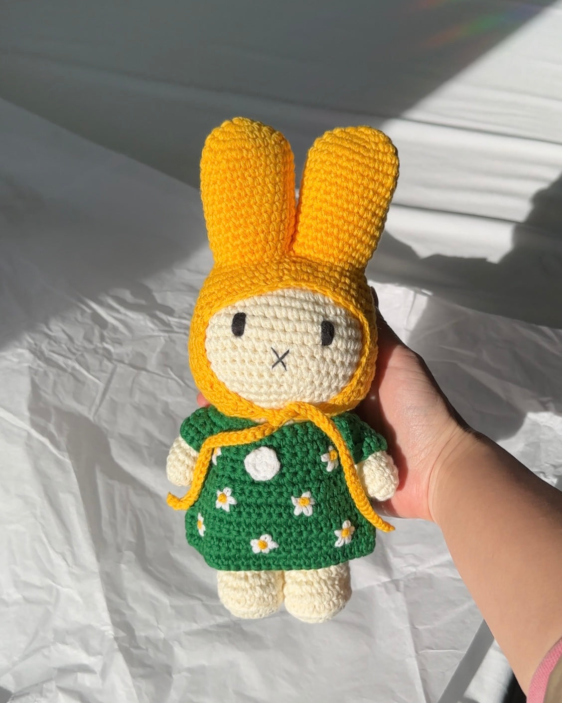 Close-up of handmade crochet Miffy bunny in yellow hood and green daisy dress
