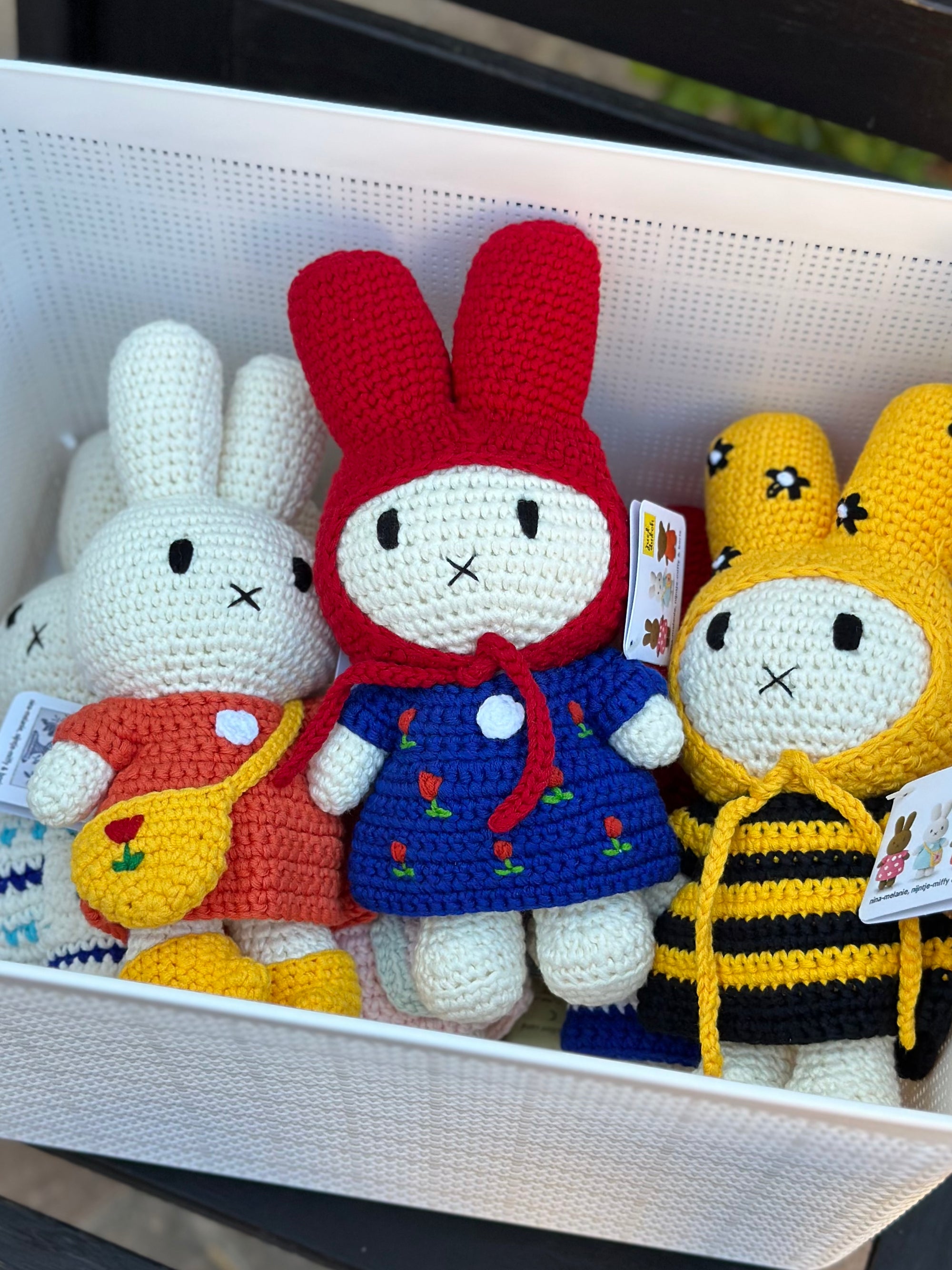 Basket of Miffy crochet dolls in different outfits including blue tulip dress, orange dress, and bee costume.