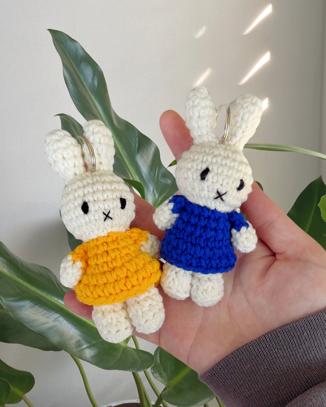 Hand-crocheted Miffy keychain in a navy blue dress held in hand next to another colorway, handmade cotton Miffy bag charm with soft texture.