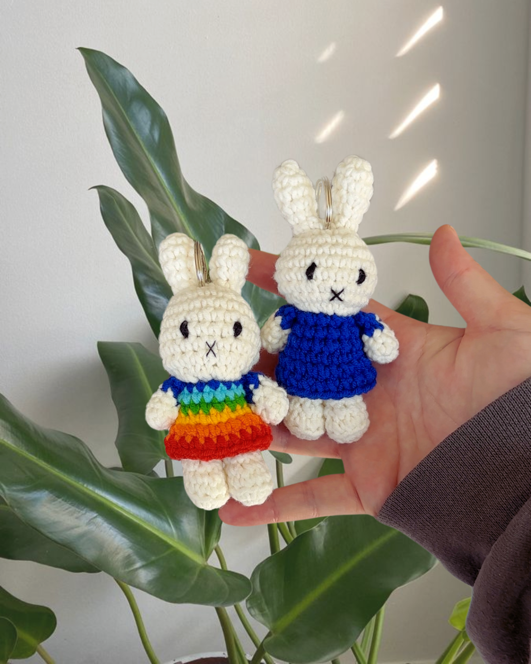 Two Miffy crochet keychains shown together, one in a navy blue dress and one in a rainbow dress, handmade cotton bag charms with metal keyrings.