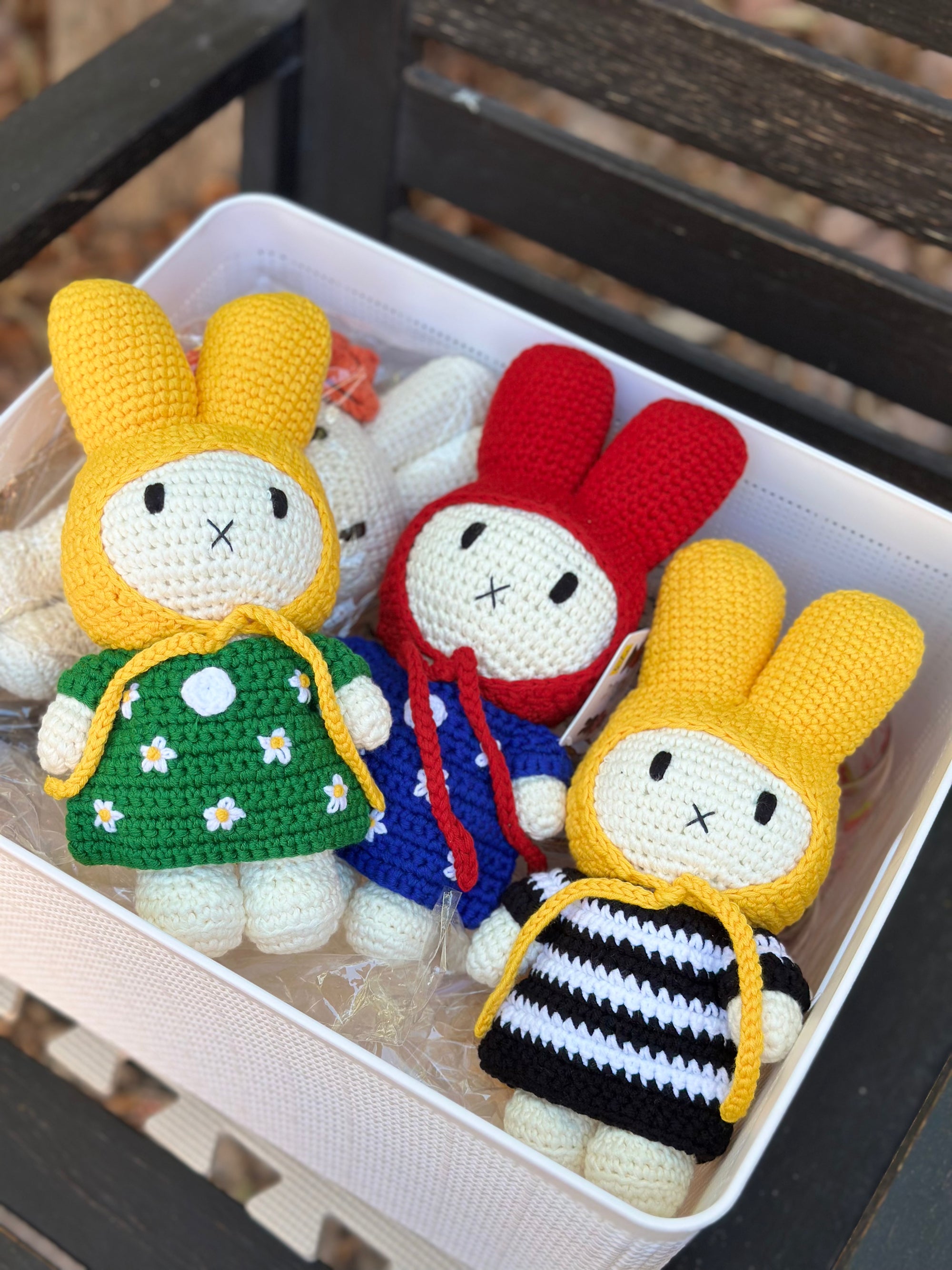 Handmade crochet Miffy bunny dolls in colorful outfits, including a green dress with daisies, blue dress with red hood, and black-and-white striped dress with yellow hood
