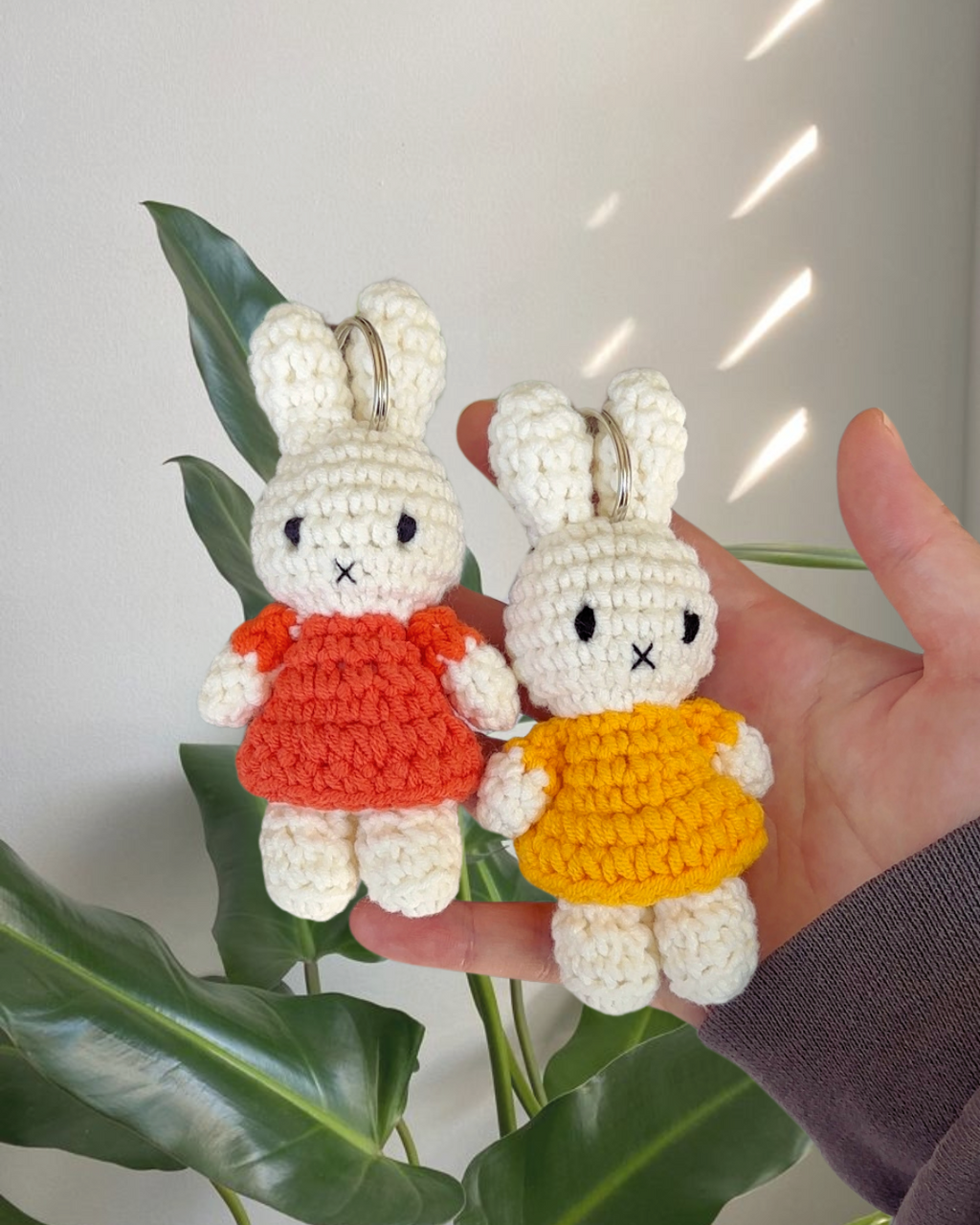 Hand-crocheted Miffy keychain in a soft yellow dress held in hand next to another colorway, handmade cotton Miffy bag charm with cozy texture.