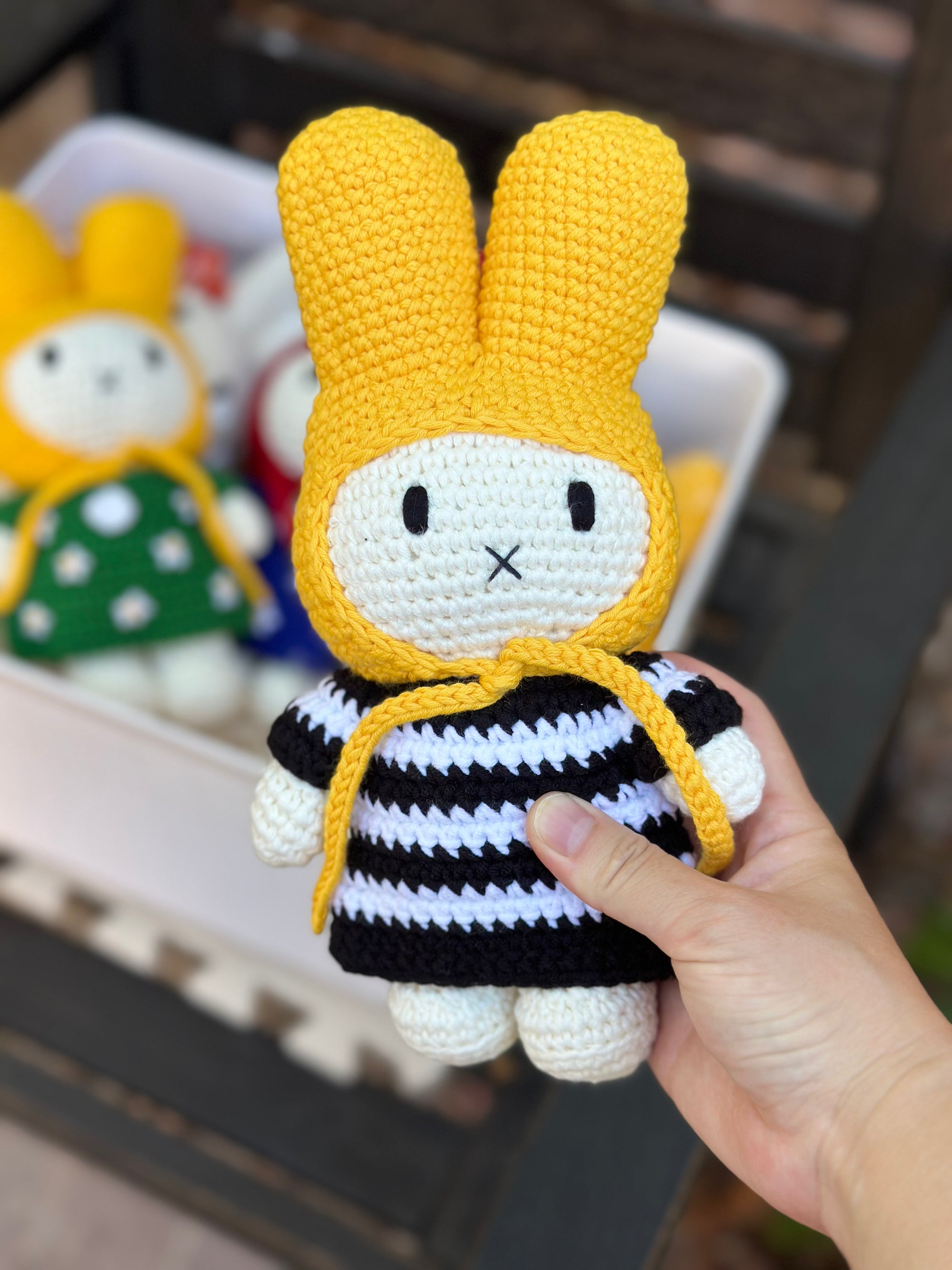 Close-up of a handmade crochet Miffy bunny doll wearing a yellow hood and black-and-white striped dress