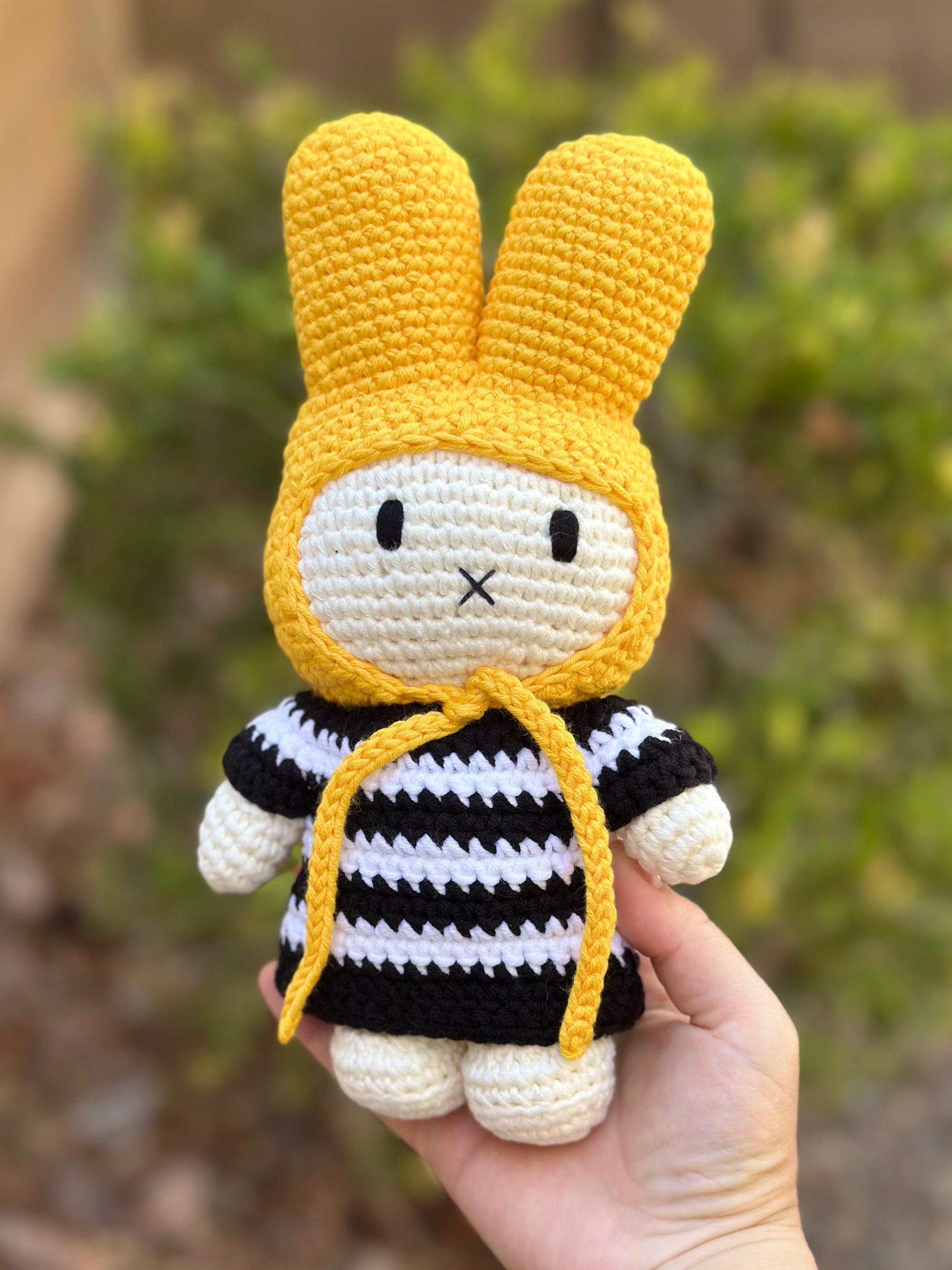 Close-up of a handmade crochet Miffy bunny doll wearing a yellow hood and black-and-white striped dress