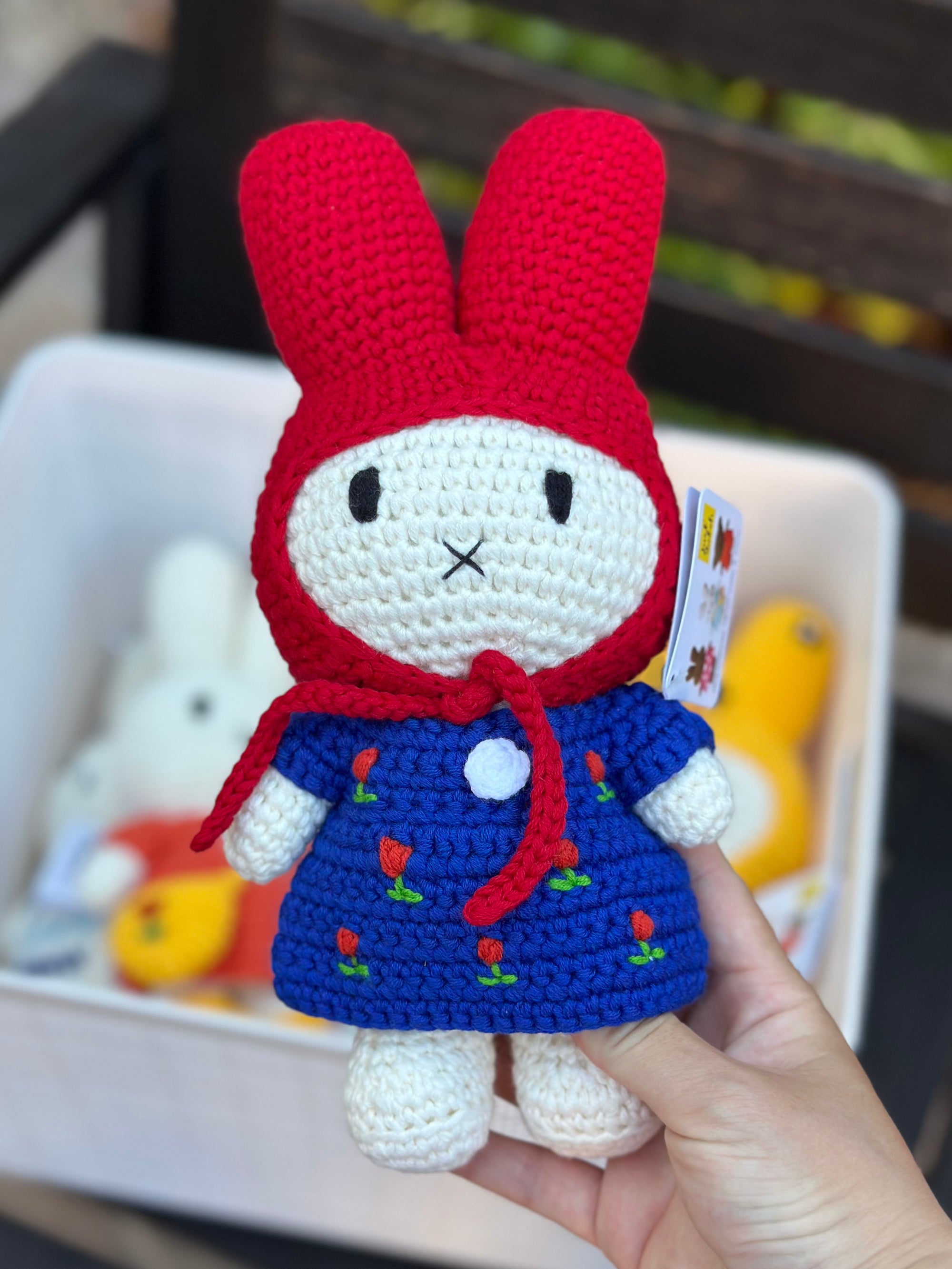 Miffy crochet doll in tulip dress and red bonnet, held above a basket of other Miffy plushies.