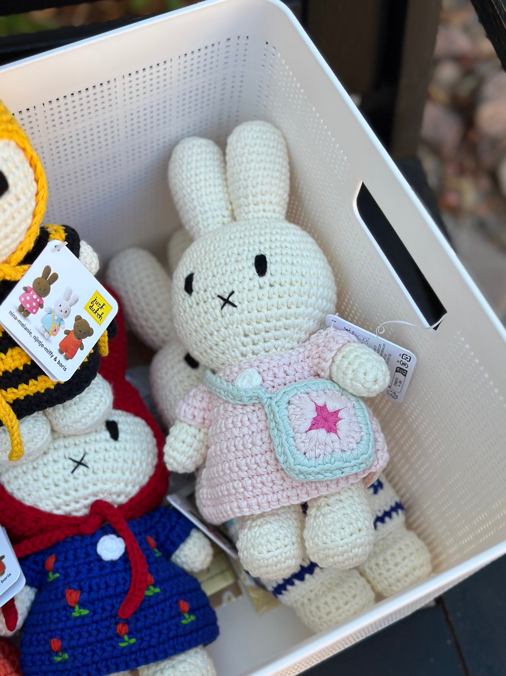 Handmade Miffy crochet plush in pink dress with a blue flower bag, sitting in a storage basket with other collectible crochet dolls.