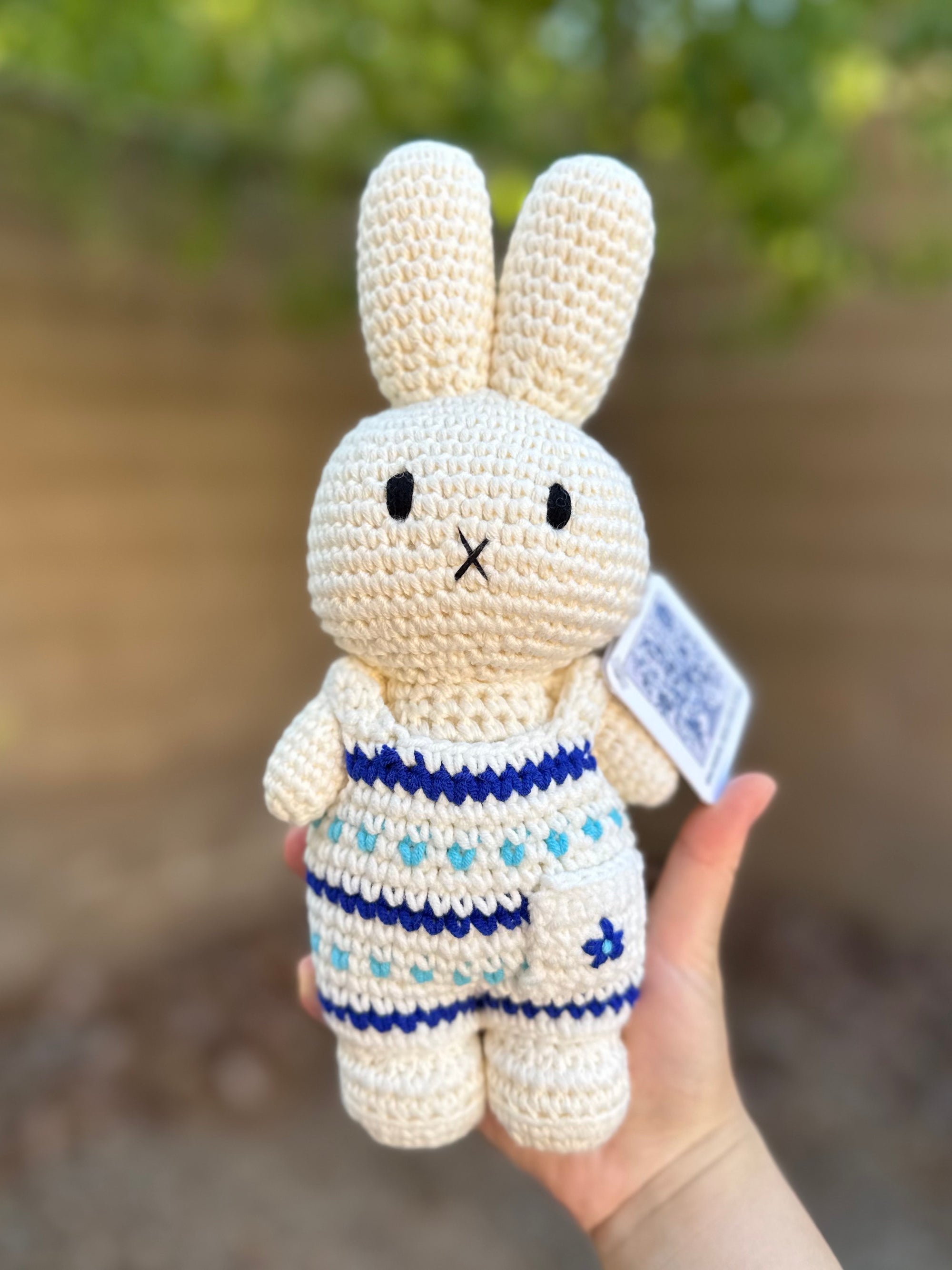 Handmade Miffy crochet plush in a Delft-inspired blue-and-white floral jumpsuit, held outdoors against a blurred background.