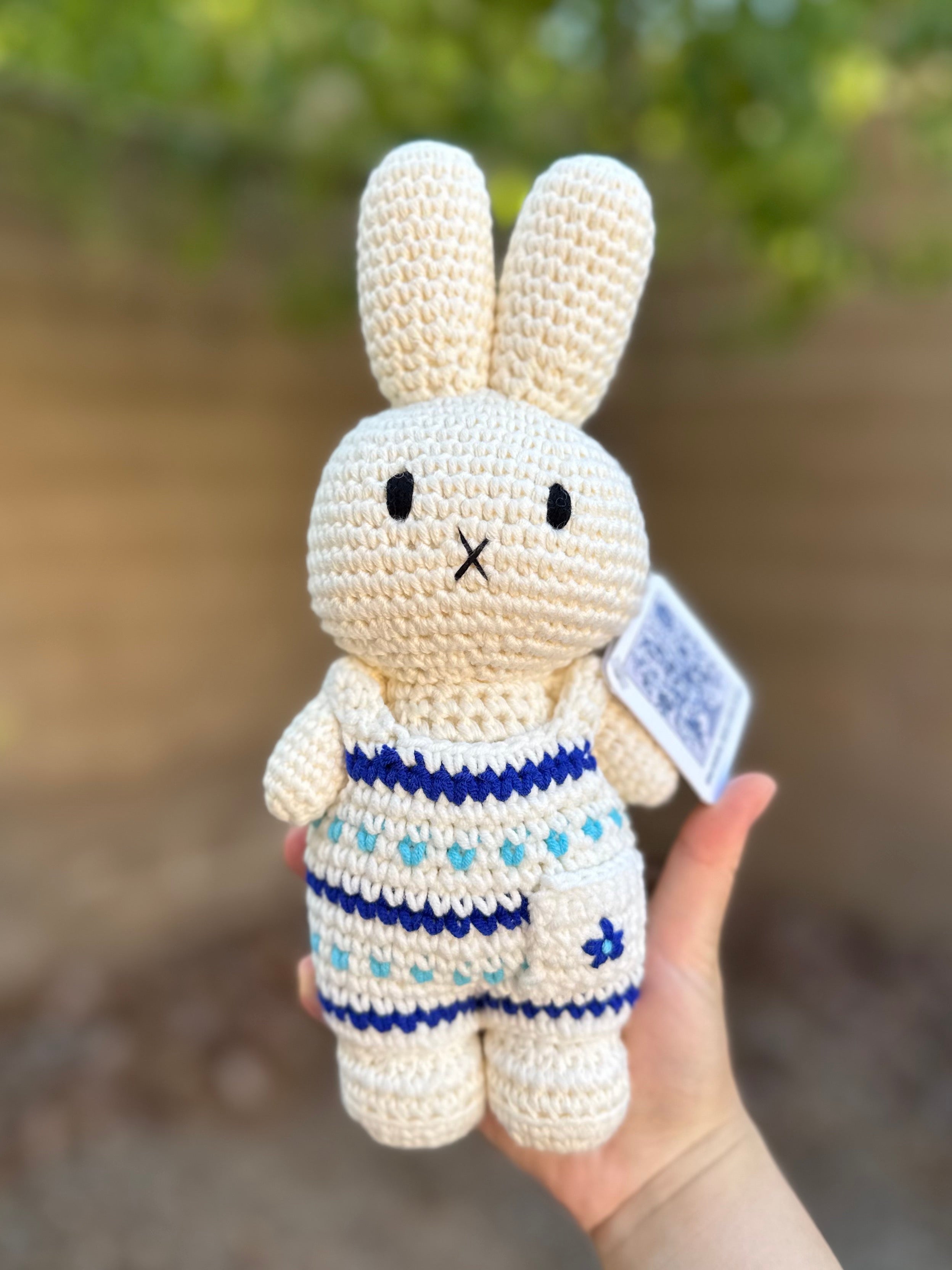 Handmade Miffy crochet plush in a Delft-inspired blue-and-white floral jumpsuit, held outdoors against a blurred background.