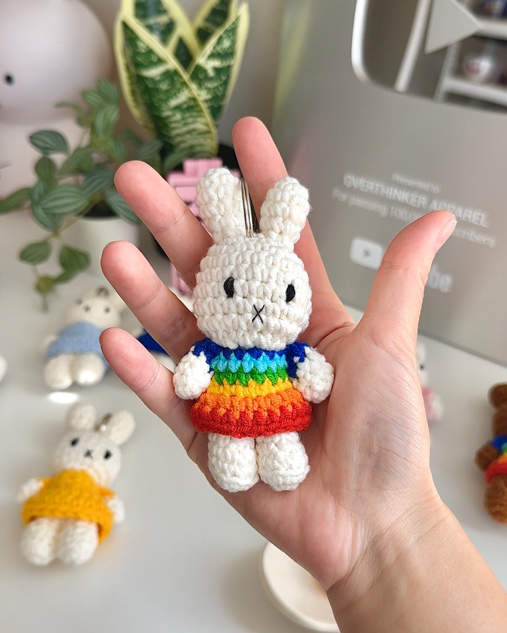 Handmade Miffy crochet keychain in a rainbow dress held in hand, soft cotton yarn texture with colorful stripes and metal keyring.