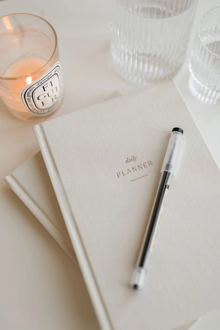 Minimal beige linen hardcover daily planner with gold foil title, styled with pen and candle for calm, neutral productivity aesthetic.
