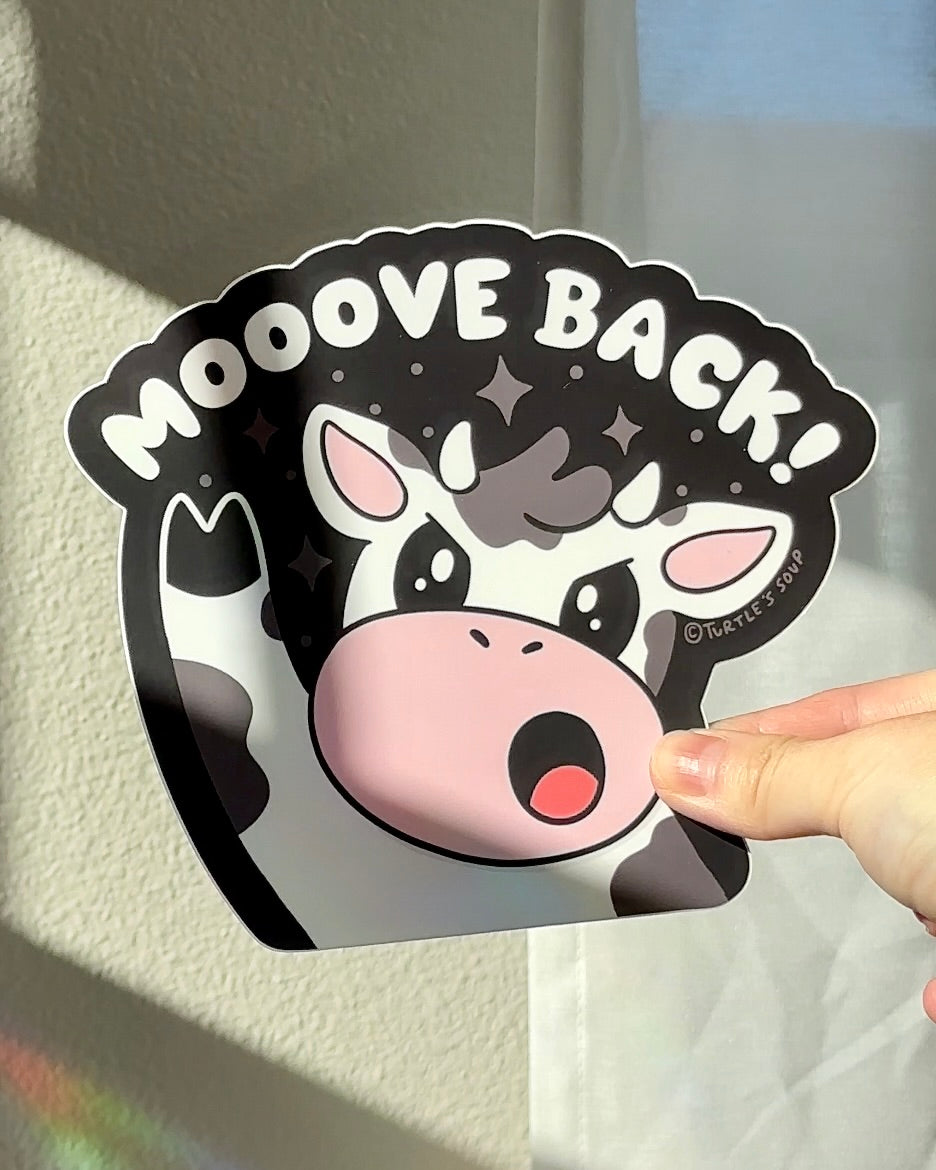 Hand holding a cute vinyl car sticker with a cow and the words “Mooove Back,” playful cottagecore tailgater decal for car bumpers.