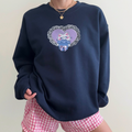 Model wearing a navy sweatshirt with a purple heart and cat patchwork embroidery design on the chest, paired with pink gingham shorts. Cozy, casual style for everyday wear.