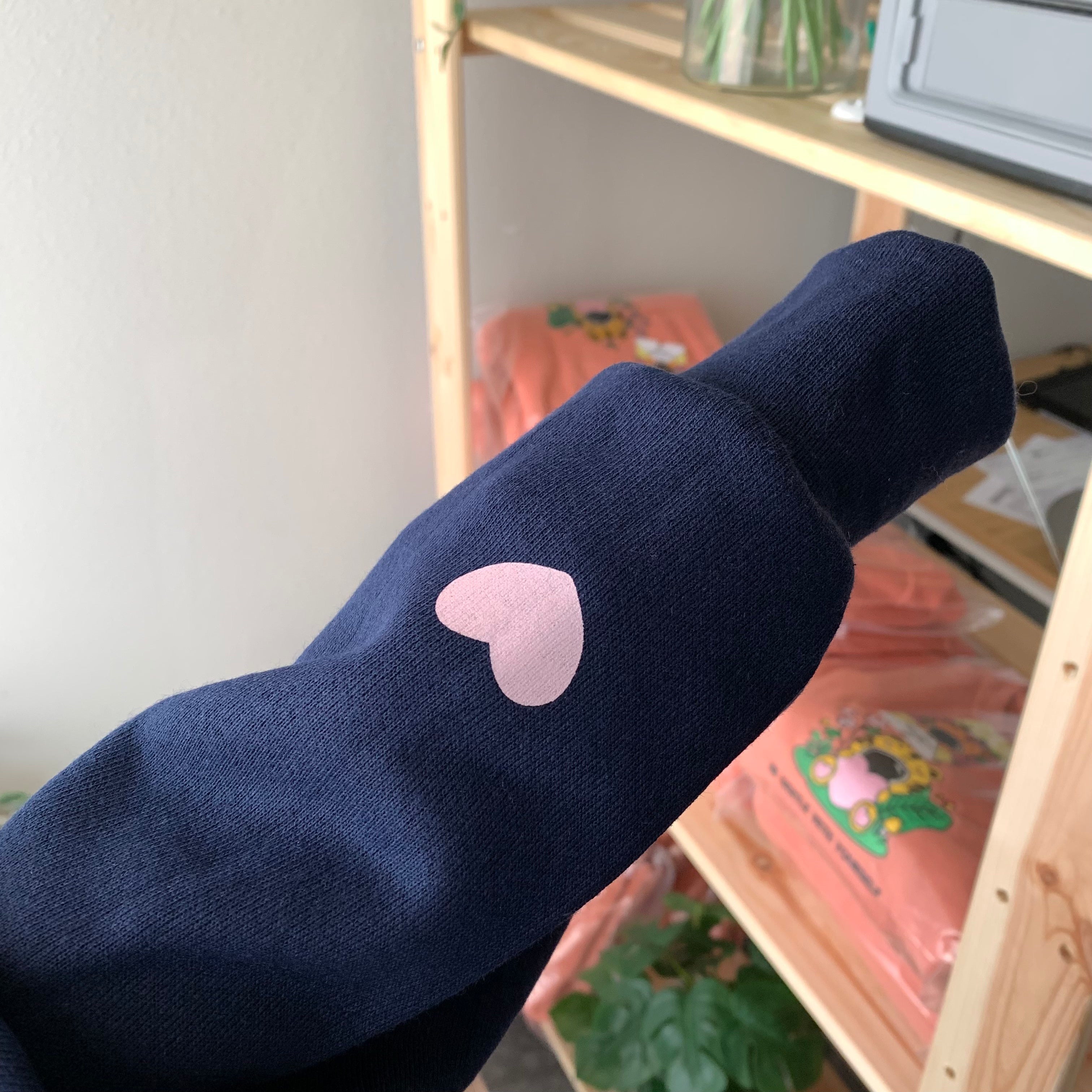 Close-up of a navy zip-up hoodie sleeve featuring a small pink heart detail, subtle affirmation clothing designed for comfort and emotional support.