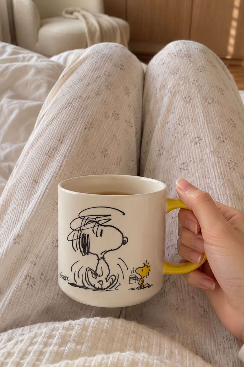 Woman holding a Snoopy Not Worth a Thing Before Coffee ceramic mug with yellow handle during a cozy morning coffee routine.
