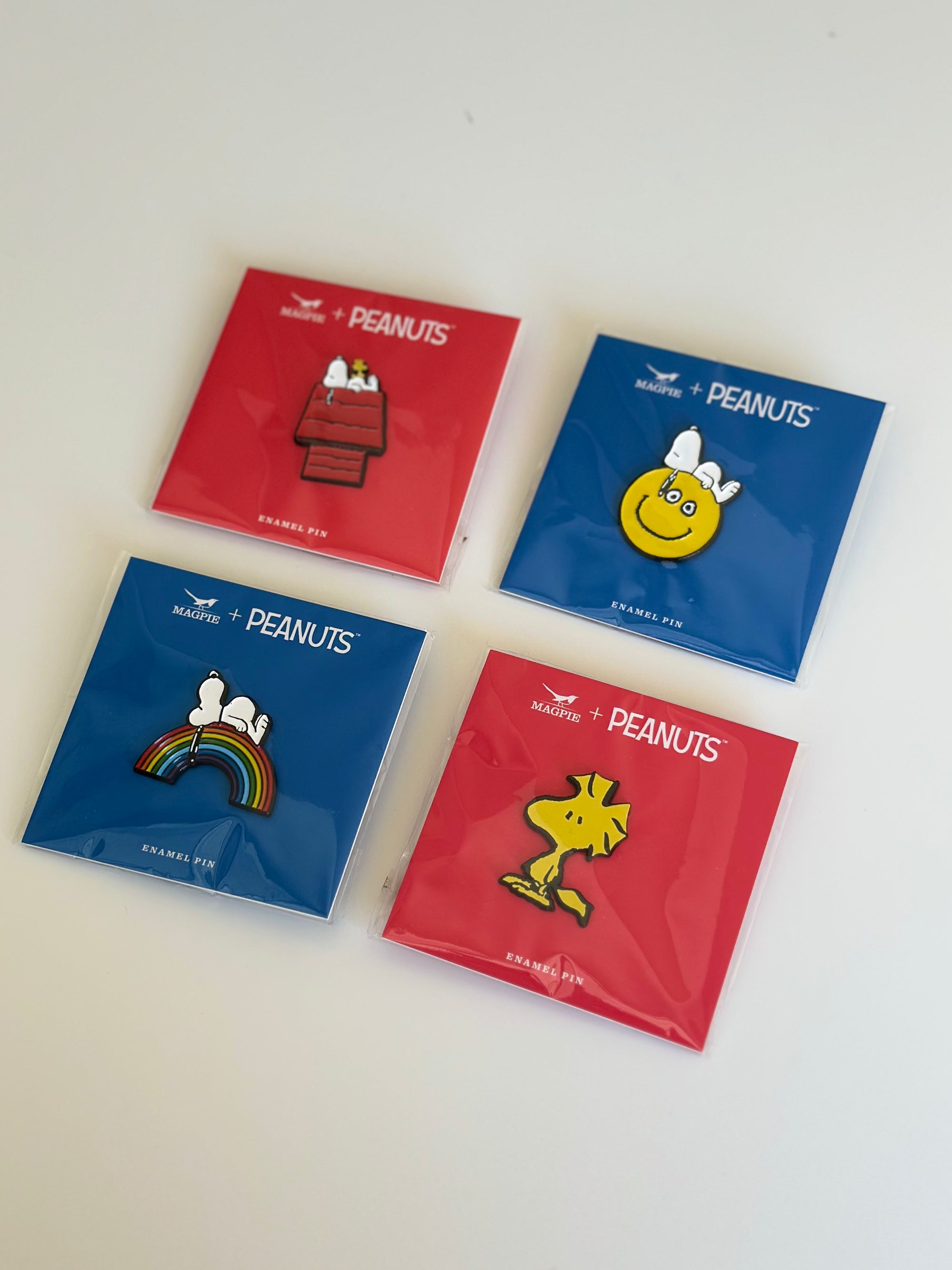 Set of 4 Peanuts® enamel pins featuring Snoopy and Woodstock on red and blue backer cards