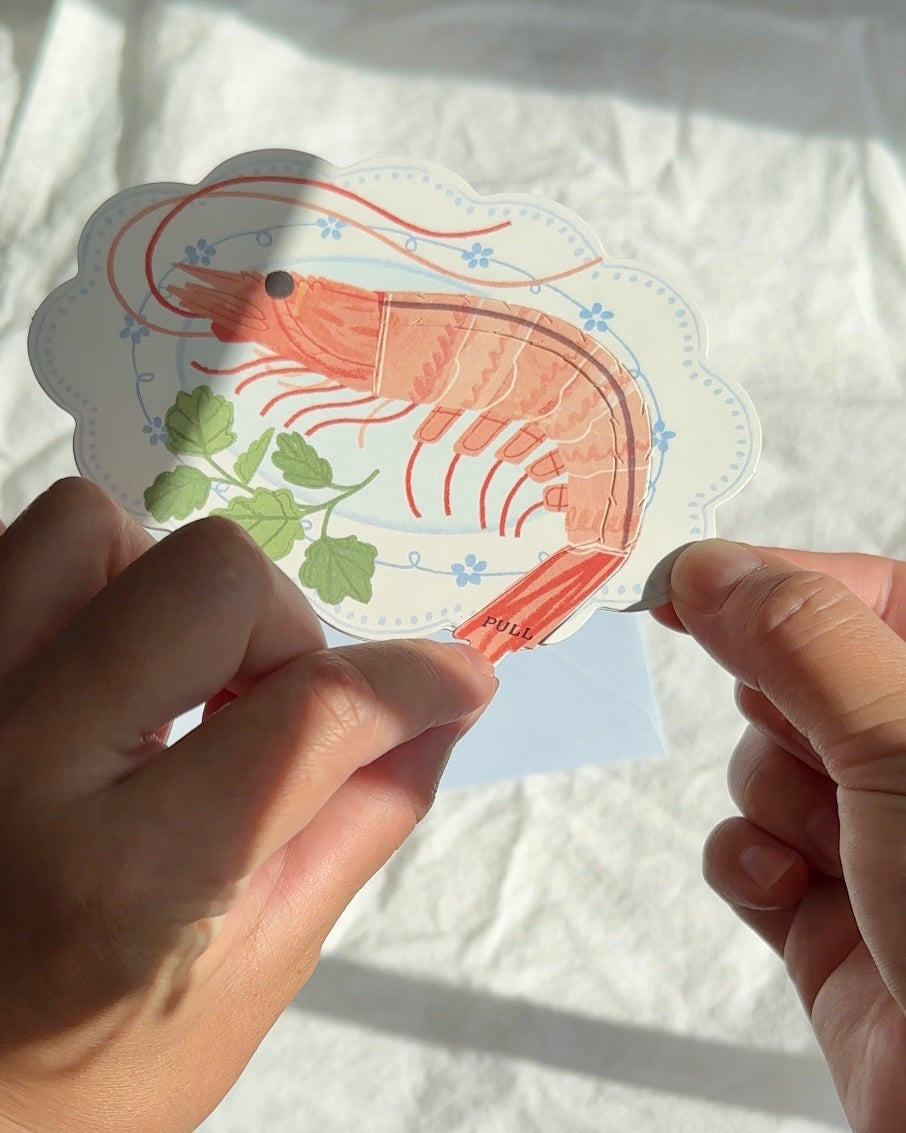 Person pulling shrimp tail tab on funny interactive greeting card.