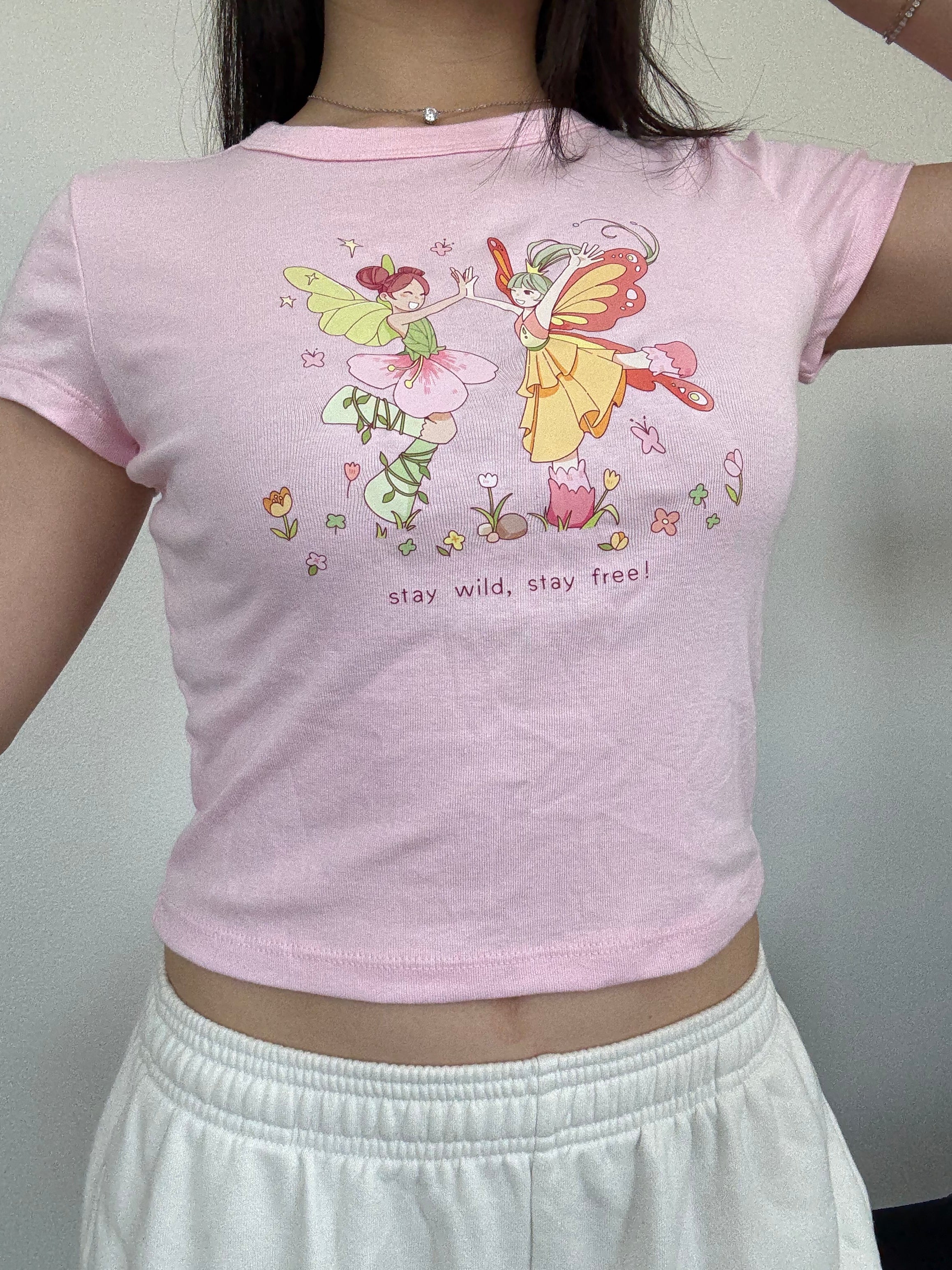 Cropped pastel pink baby tee with whimsical dancing fairy artwork and floral details