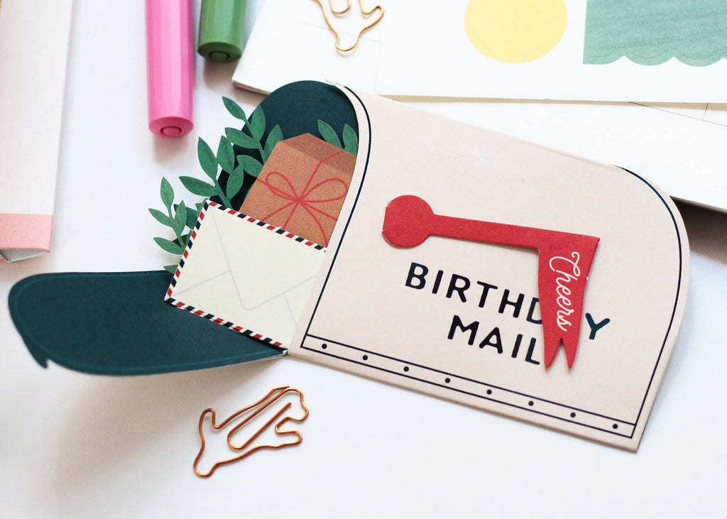 Whimsical pop-up birthday card shaped like a mailbox with “Cheers” flag, filled with 3D paper gifts, greenery, and a tiny envelope. A sweet and thoughtful birthday greeting card for friends or loved ones.

