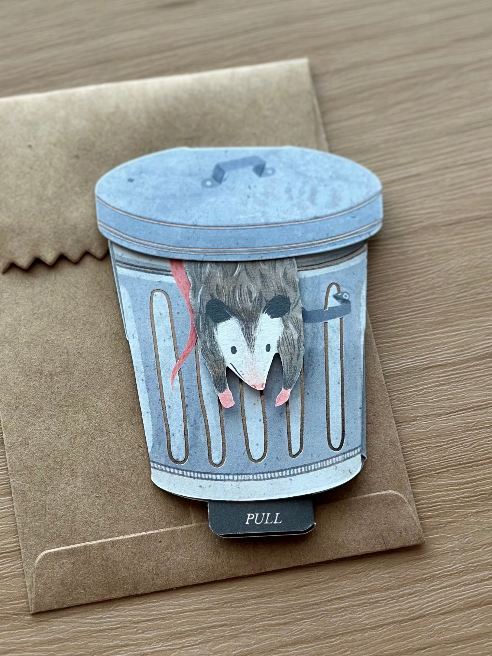 Interactive possum birthday card shaped like a trash can with pull tab feature, handmade quirky greeting card.