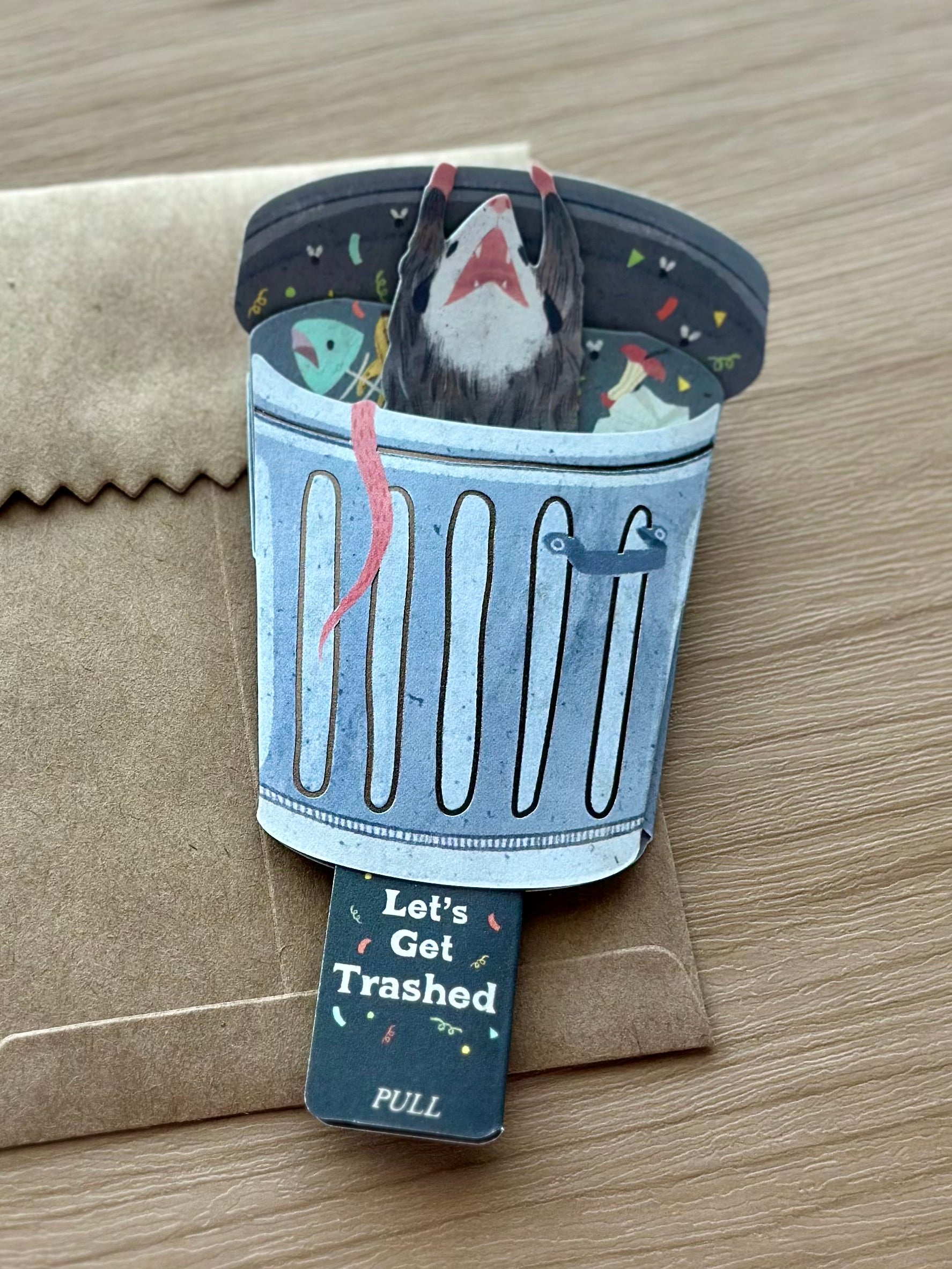 Handmade interactive birthday card with possum inside trash can and pull tab revealing “Let’s Get Trashed.”