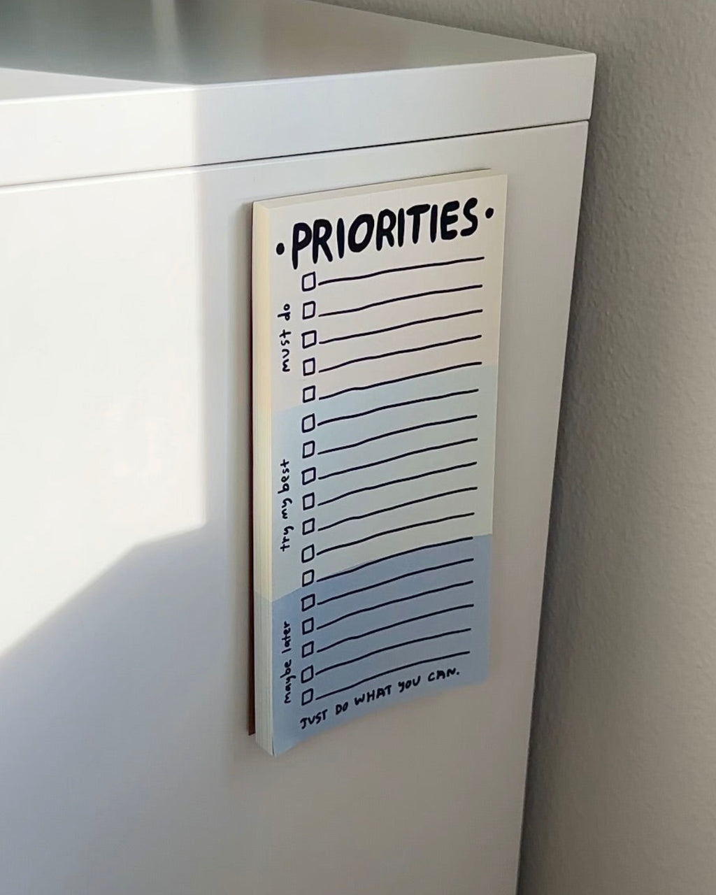 Magnetic priorities notepad hanging on a white fridge, featuring a gentle to-do list layout with sections for must do, try my best, and maybe later.