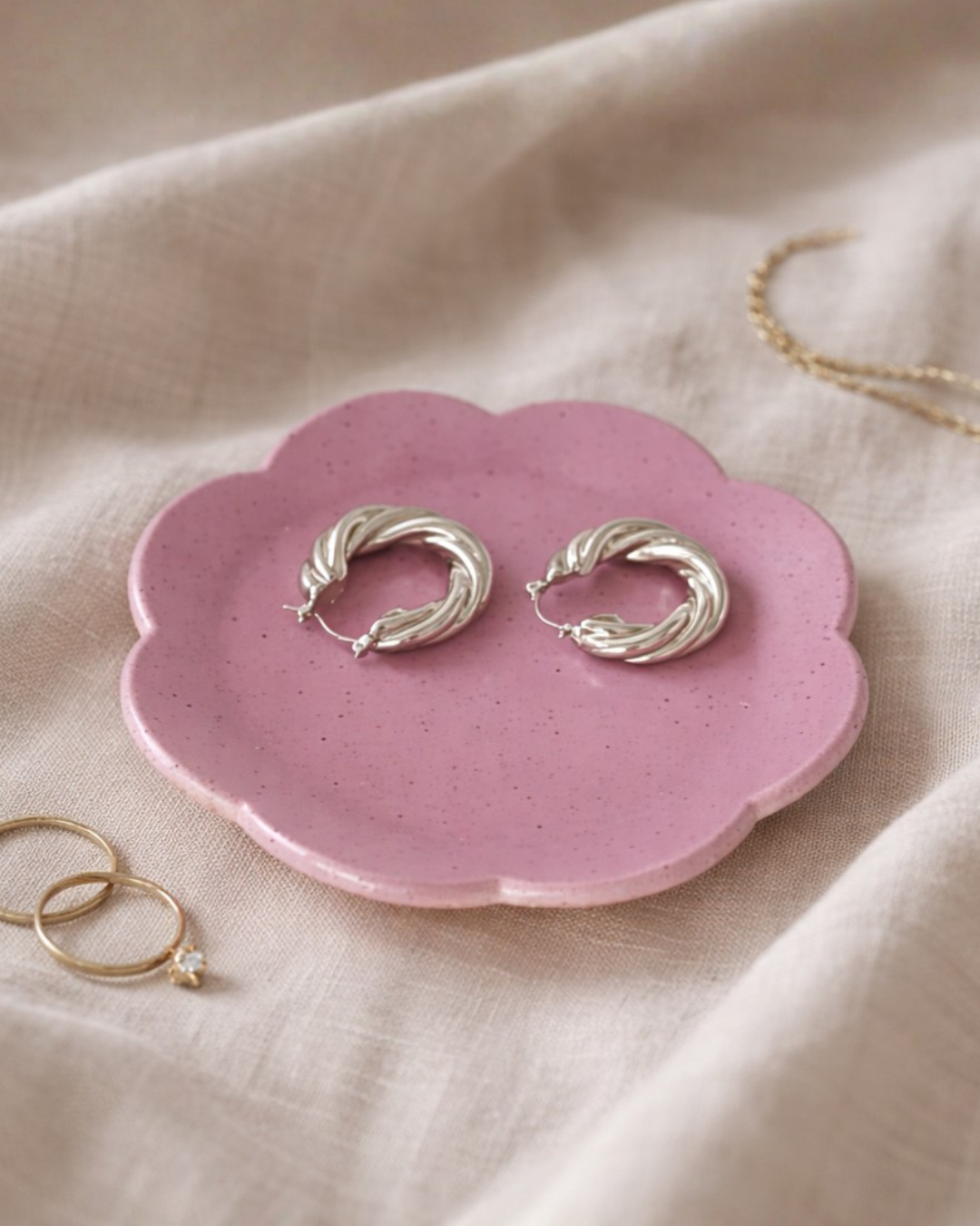 Handmade purple flower ceramic ring dish holding gold hoop earrings on soft linen fabric, cute trinket tray for vanity or bedside table
