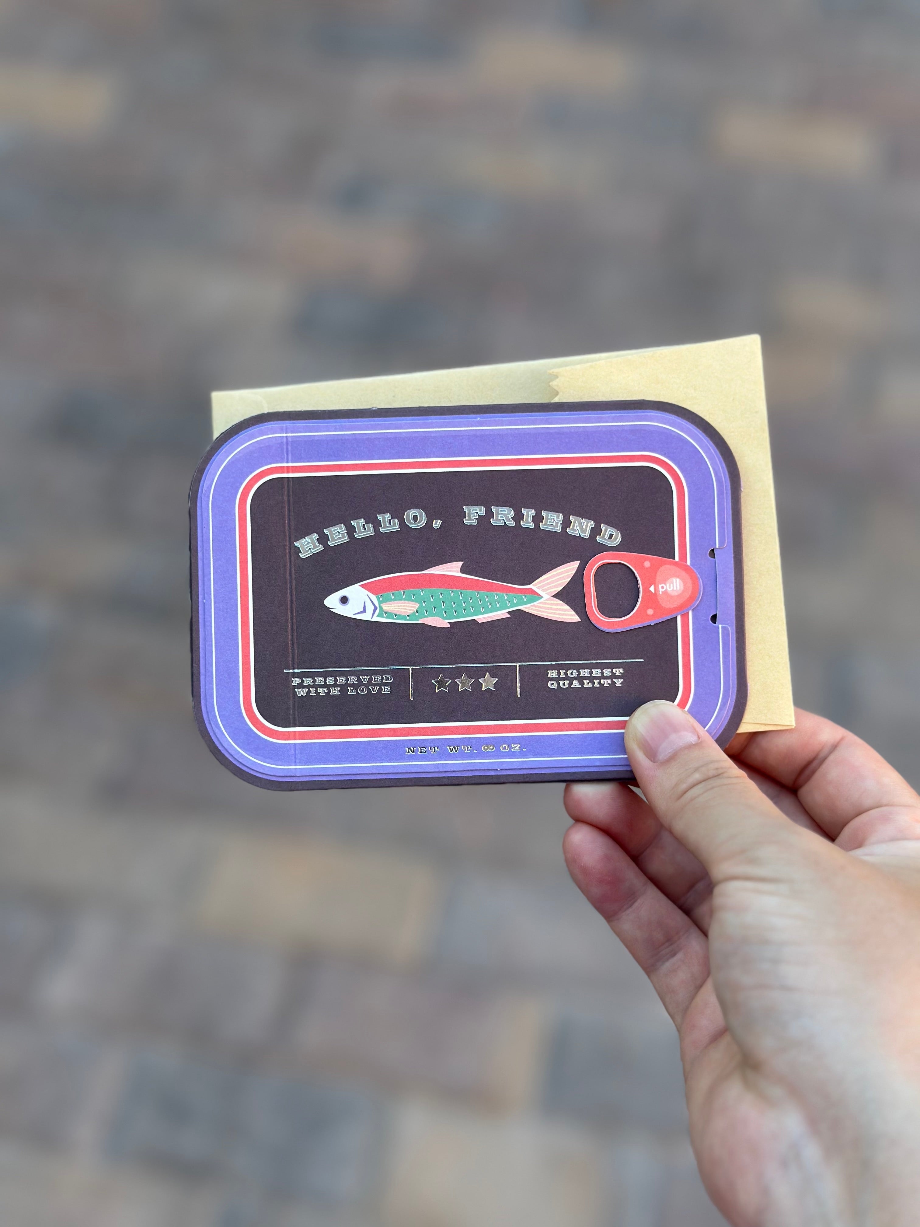 Interactive sardine tin greeting card being held with envelope, “Hello, Friend” on front.