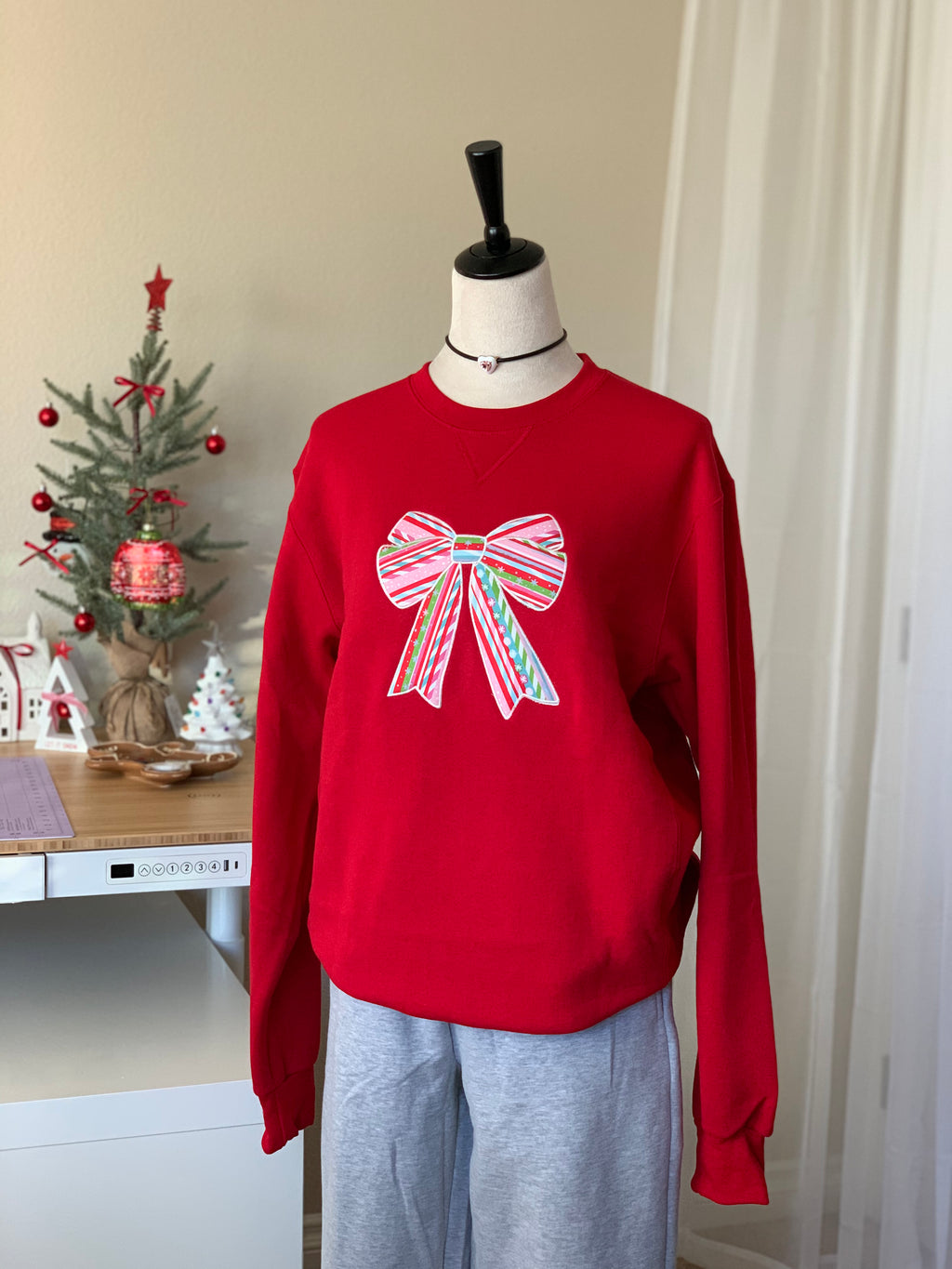 Full view of red candy-cane bow sweatshirt in bright natural light
